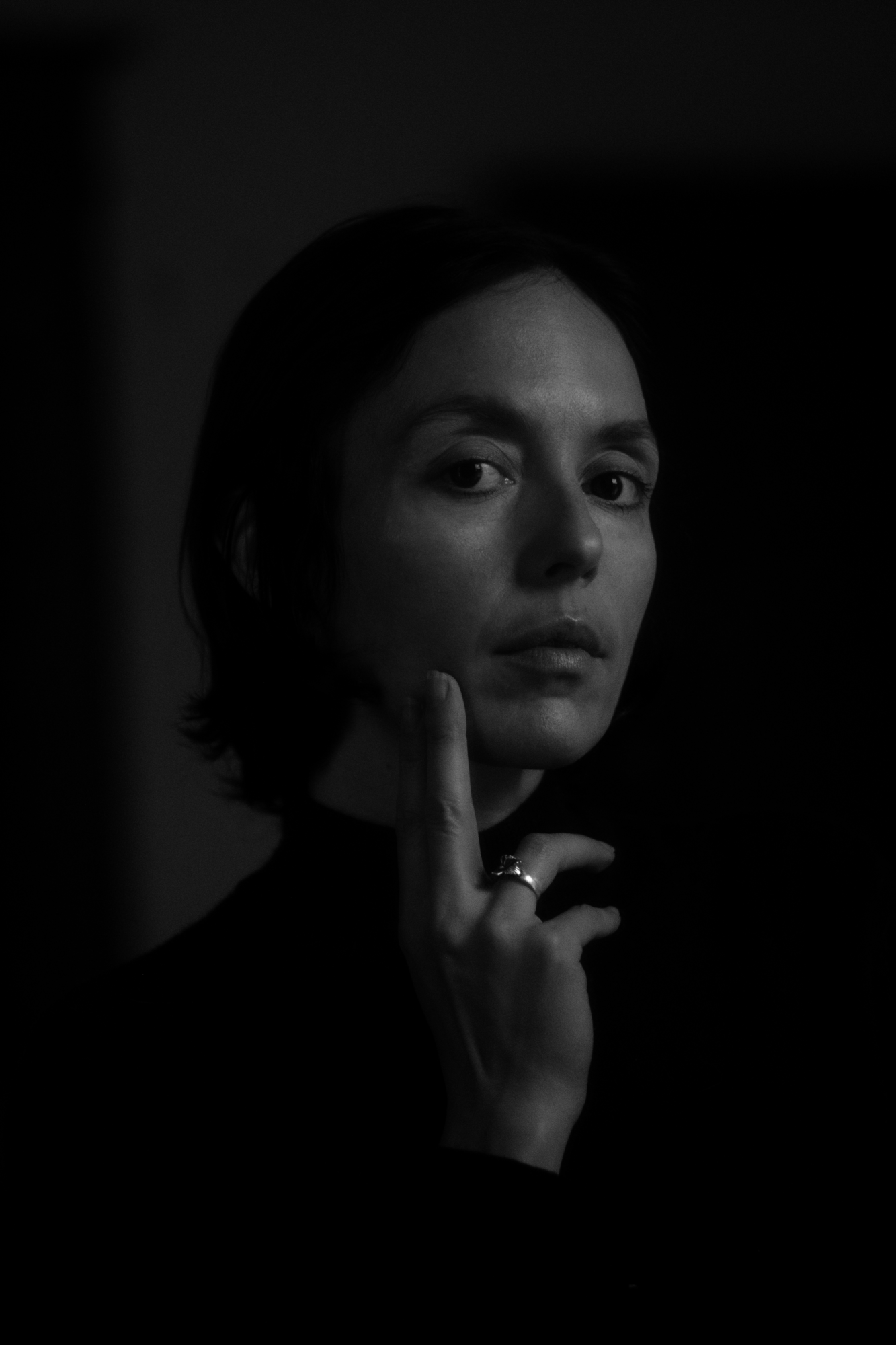 A portrait of the filmmaker, Zia Anger. Anger is shown in a dramatic, black-and-white pose, gazing at the viewer. Angers right middle finger is pressed to her chin.