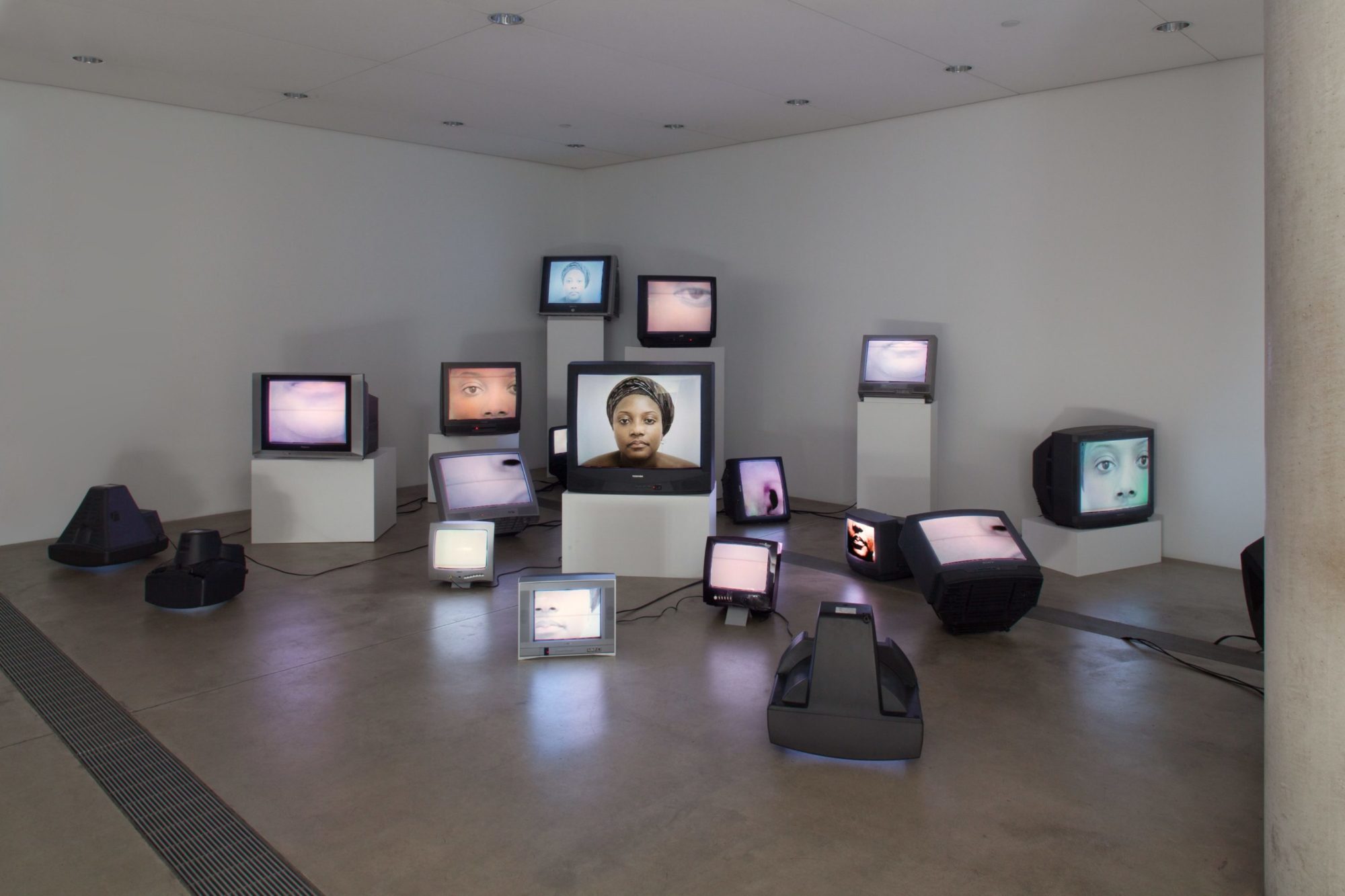 televisions of various sizes are arranged in a corner display images of a person's facial features