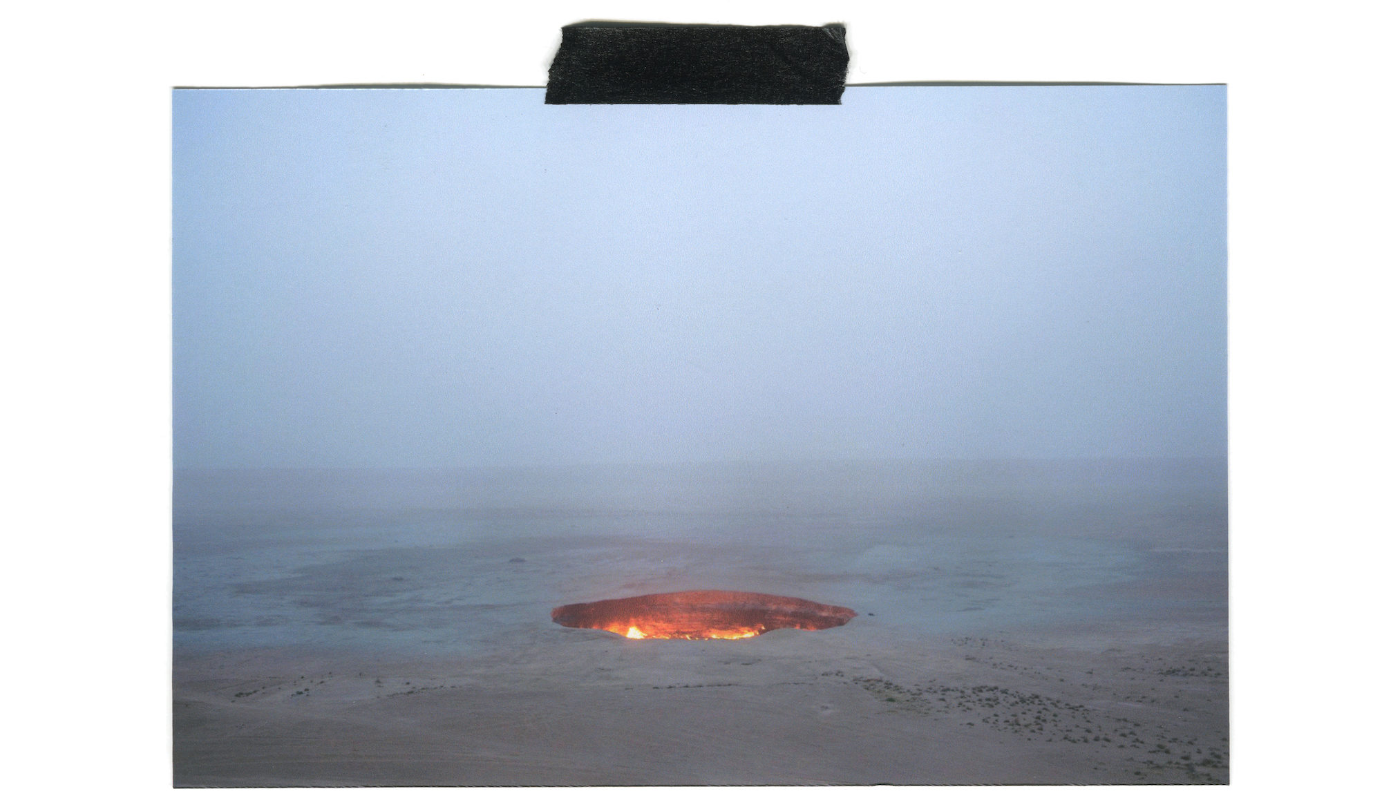 Image of the Darvaza Gas Crater in Turkmenistan held to a white wall with a piece of black tape.