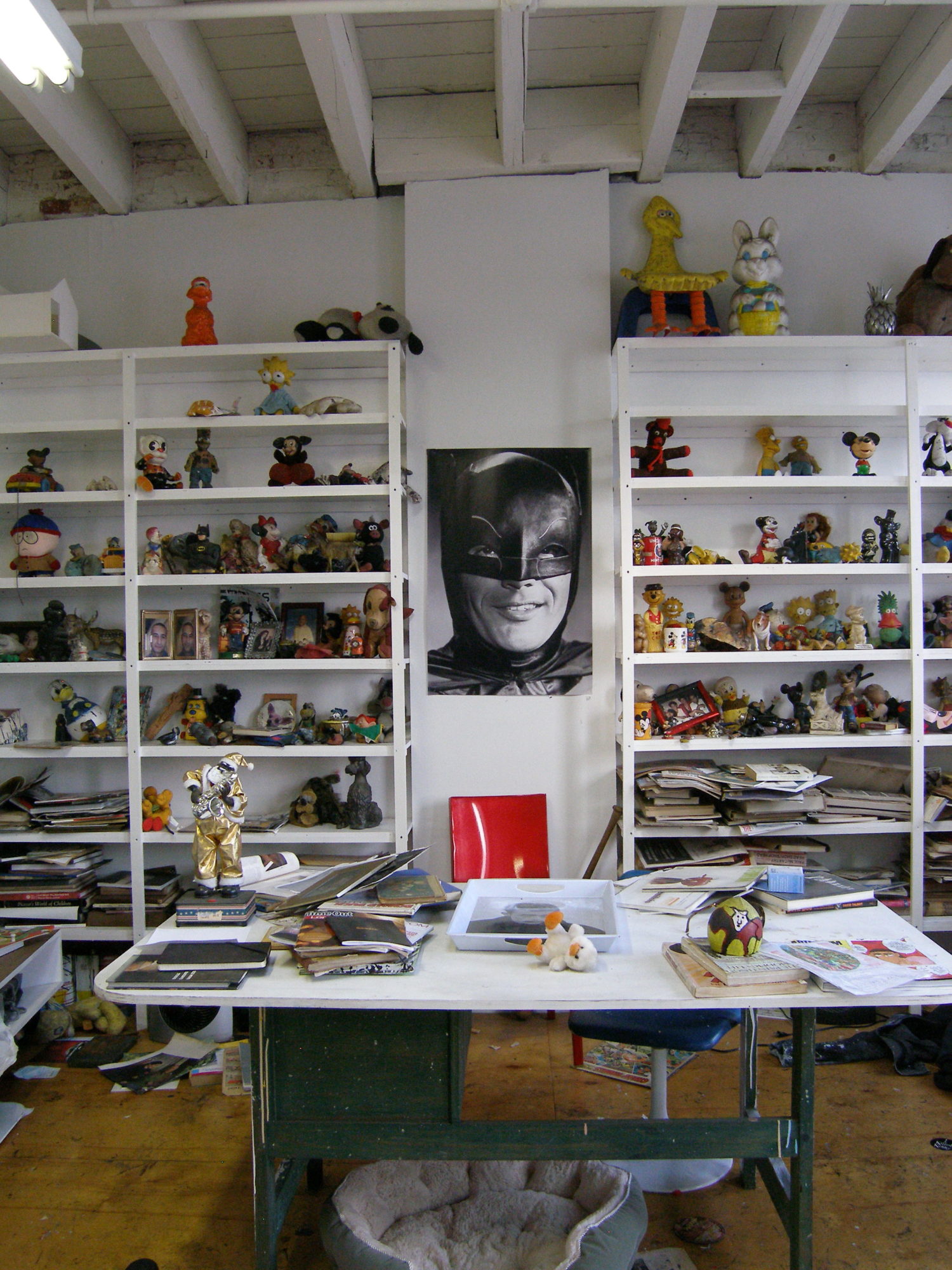 Photograph of artist's studio. Very cluttered, with papers and toys and art material strewn about shelves and tables.