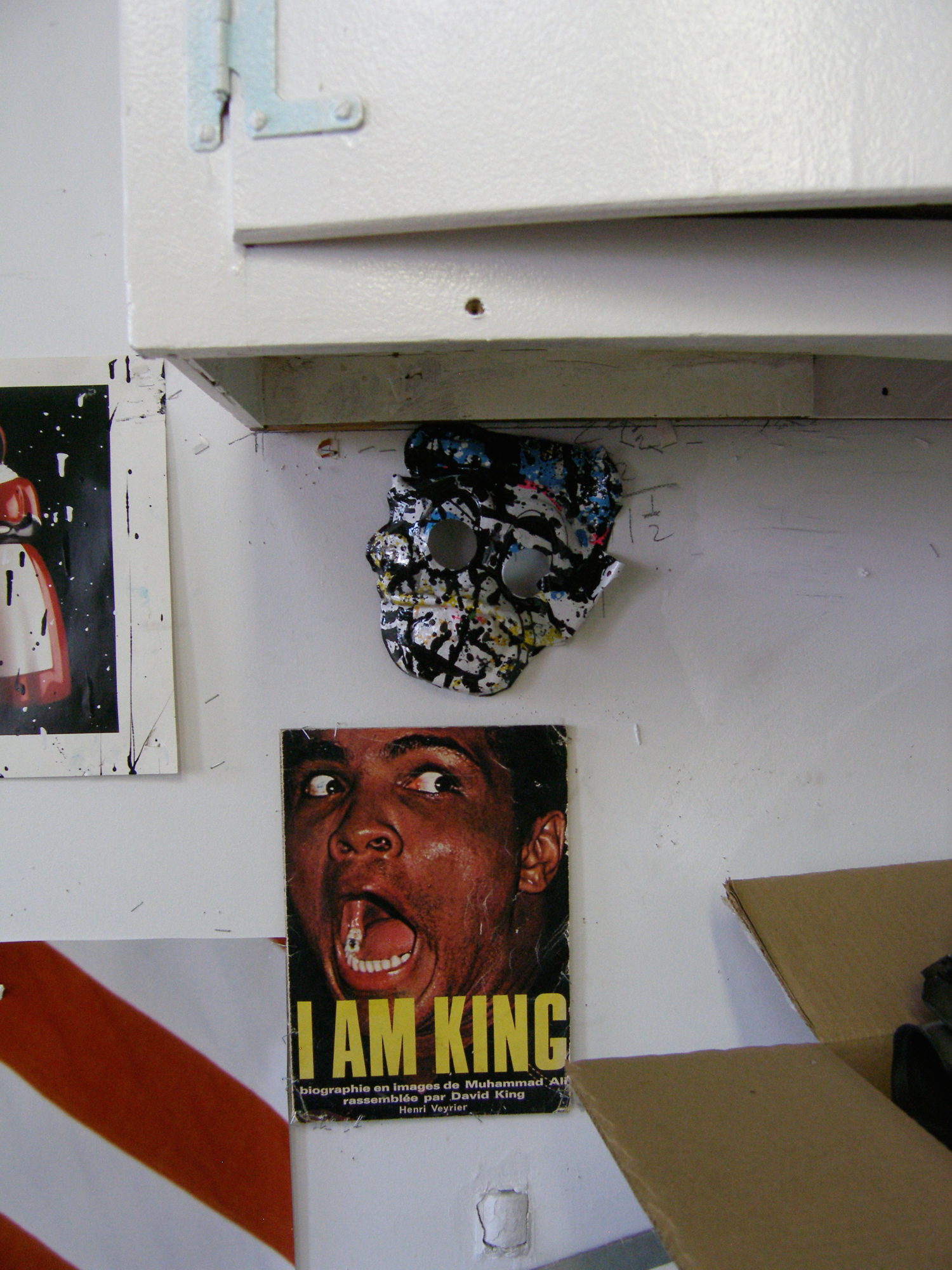 Photo of the artists studio with a skull mask and pictures hanging under a cabinet on the wall.