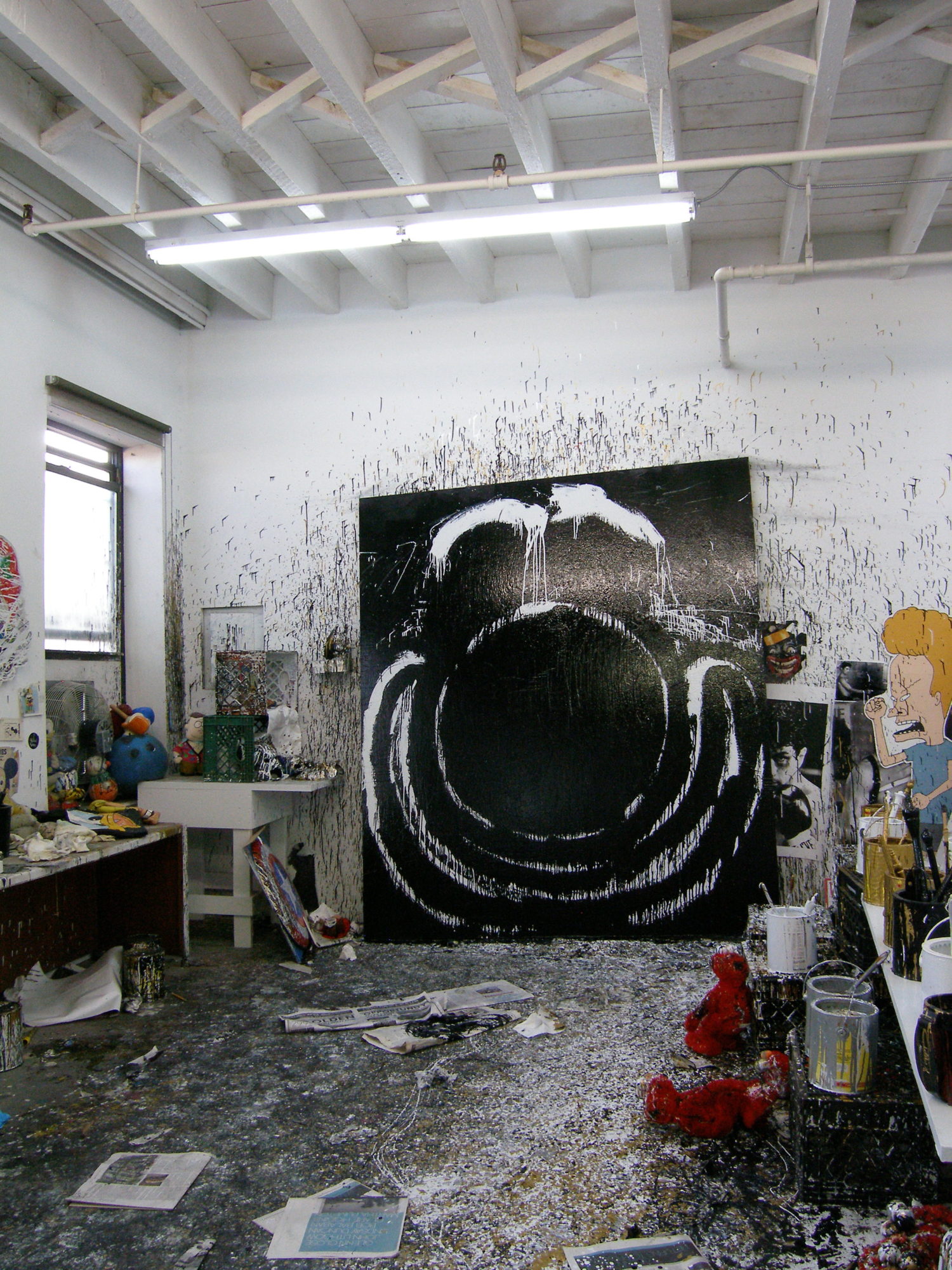 Photo focuses on a view of a cluttered art studio filled with paintings, cartoons, toys and other materials.