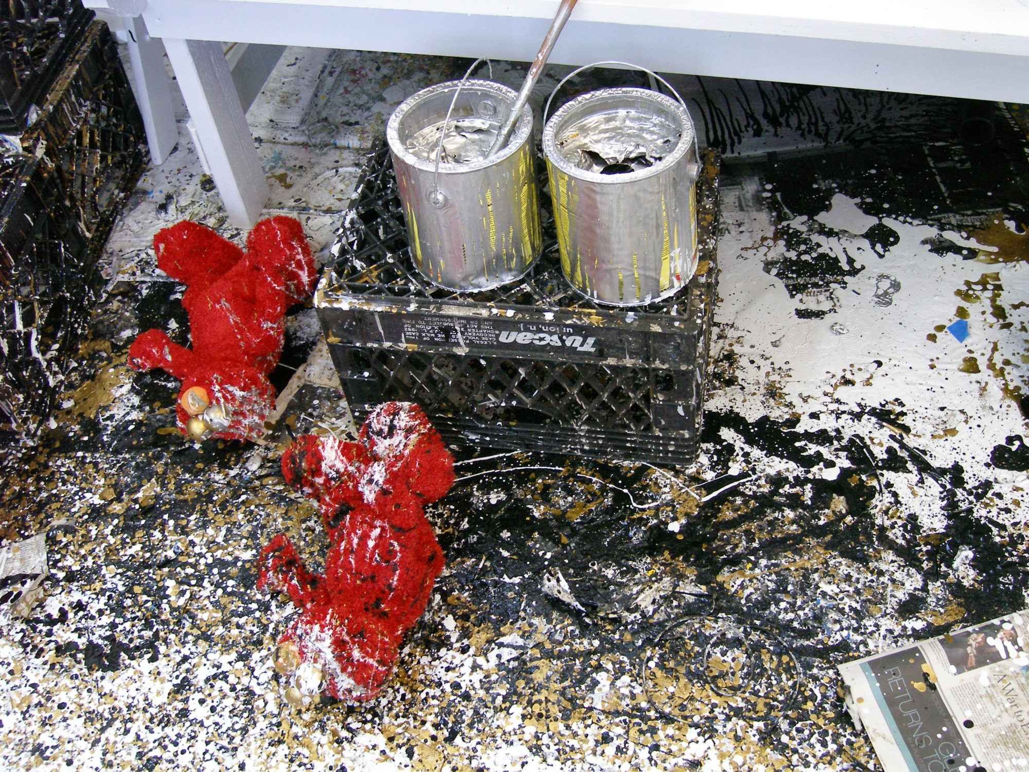 Photo contains two large elmo toys with one black crate and 2 silver paintcans splattered in gold, white and black paint.