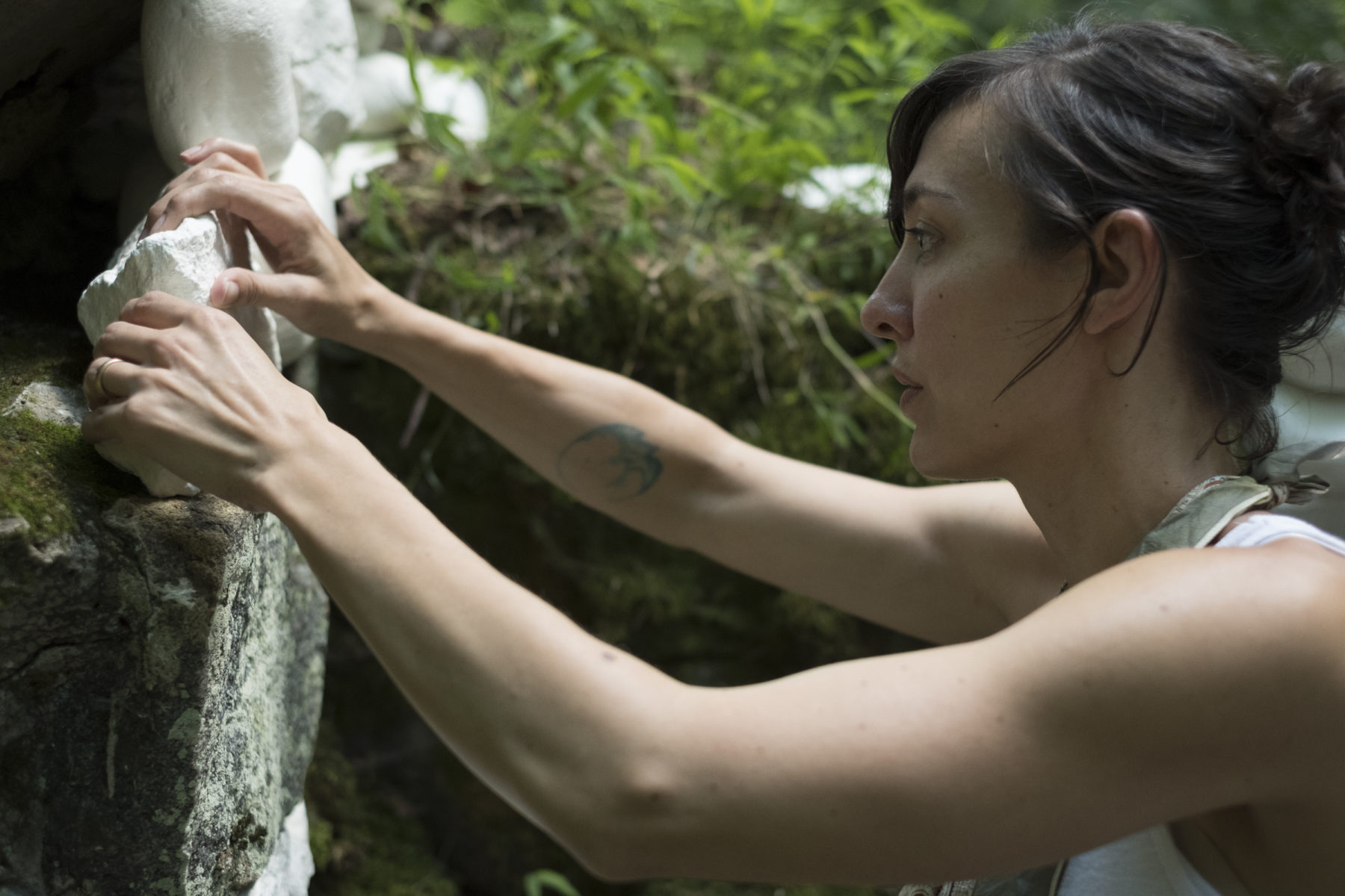 The artist in profile, Rachel, carefully places a porcelain rock on top on an existing rock
