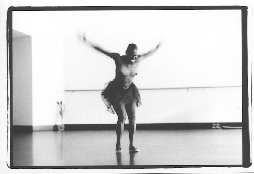a topless dancer in ballet tutu stands with arms flailing