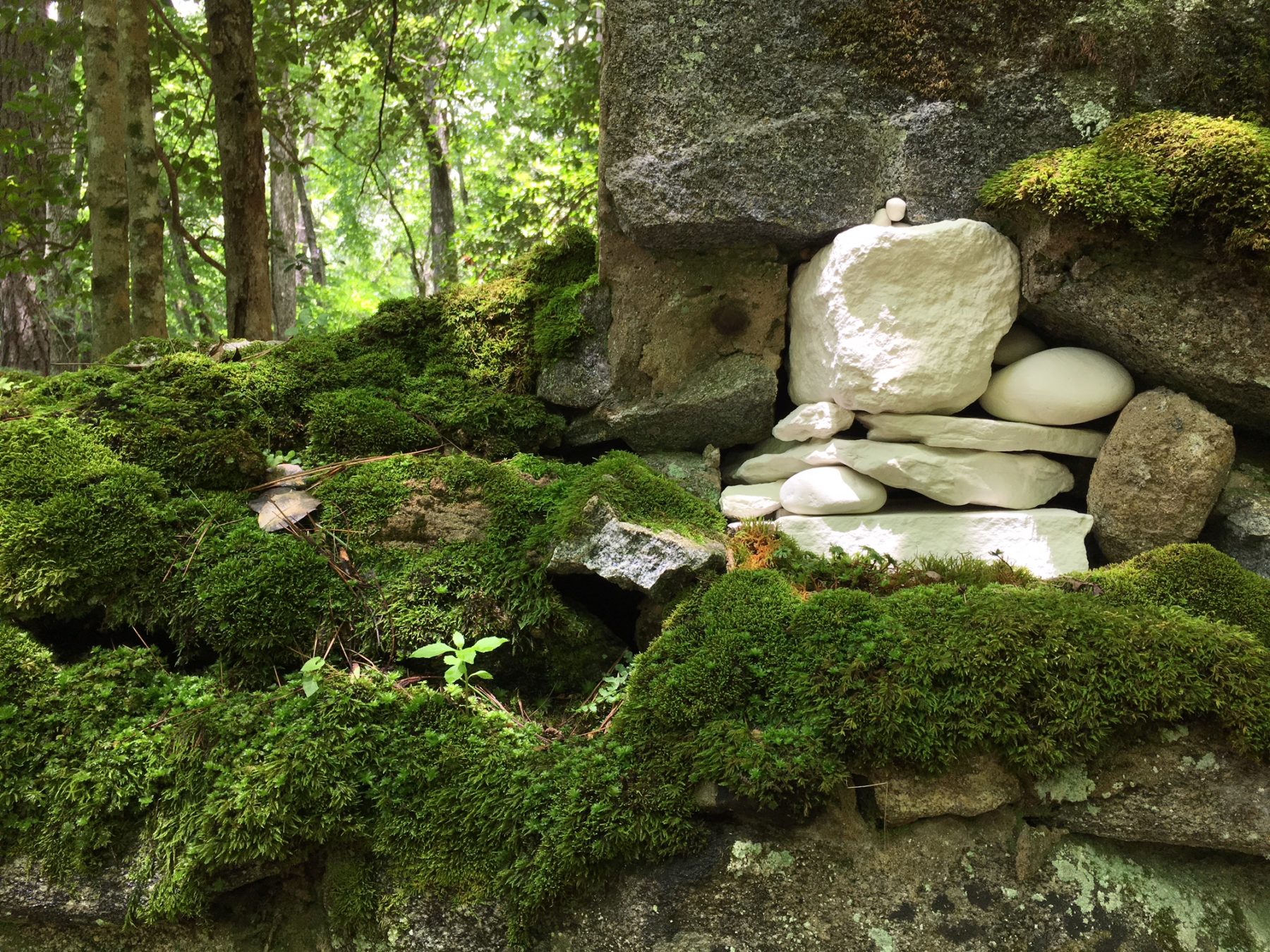 a green mossy rock structure is interrupted by a stack of perfectly white porcelain rocks by Rachel K. Garceau