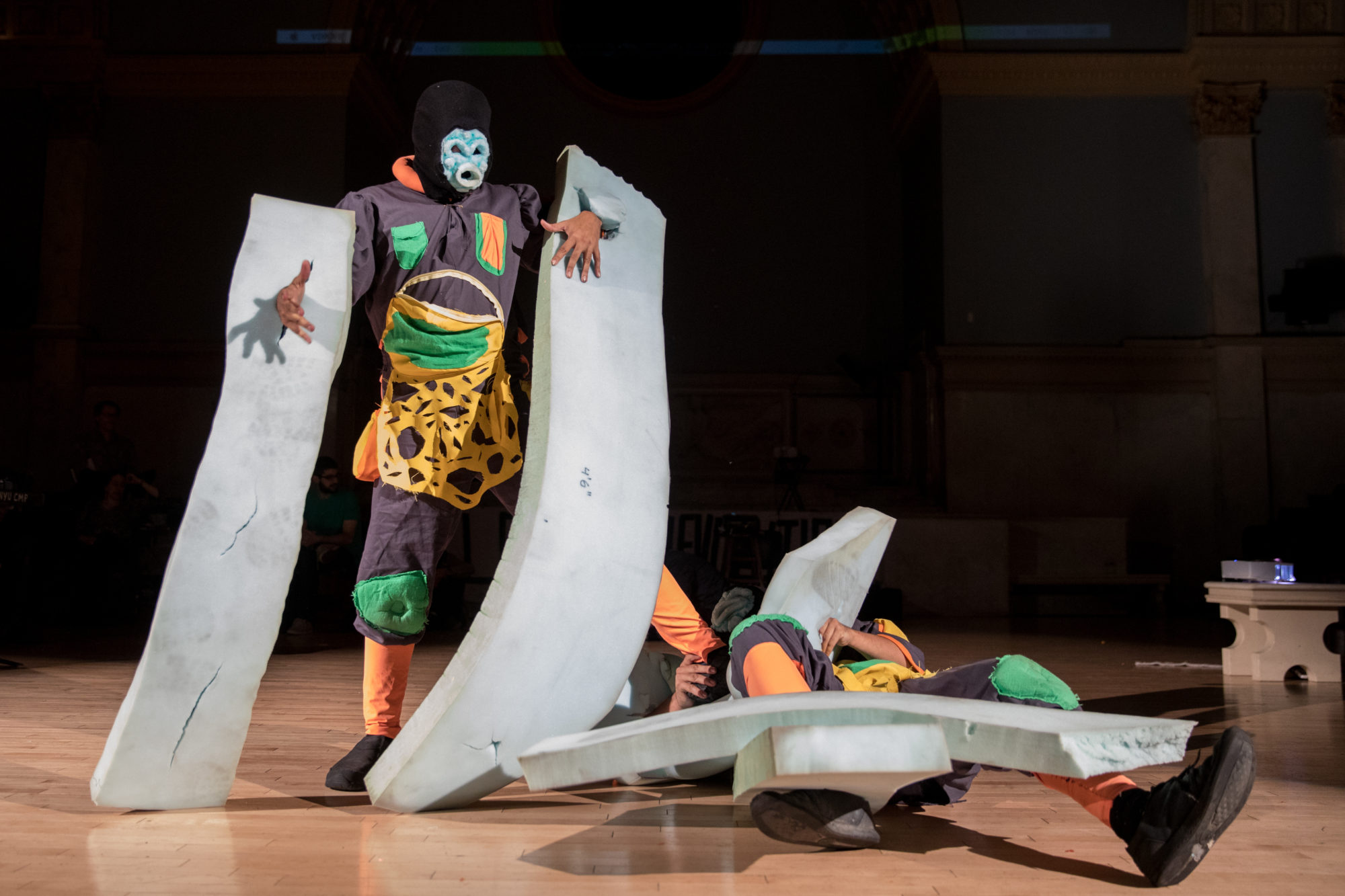 people in costumes perform on stage with blue foam pieces