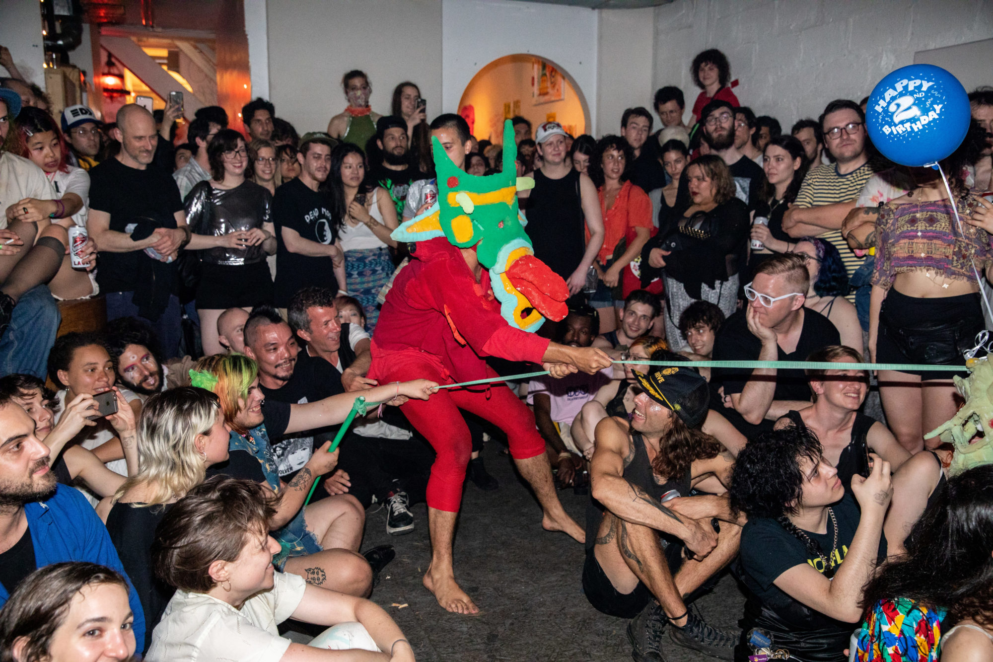 person in red clothing and a dragon mask pulls string in crowd of people