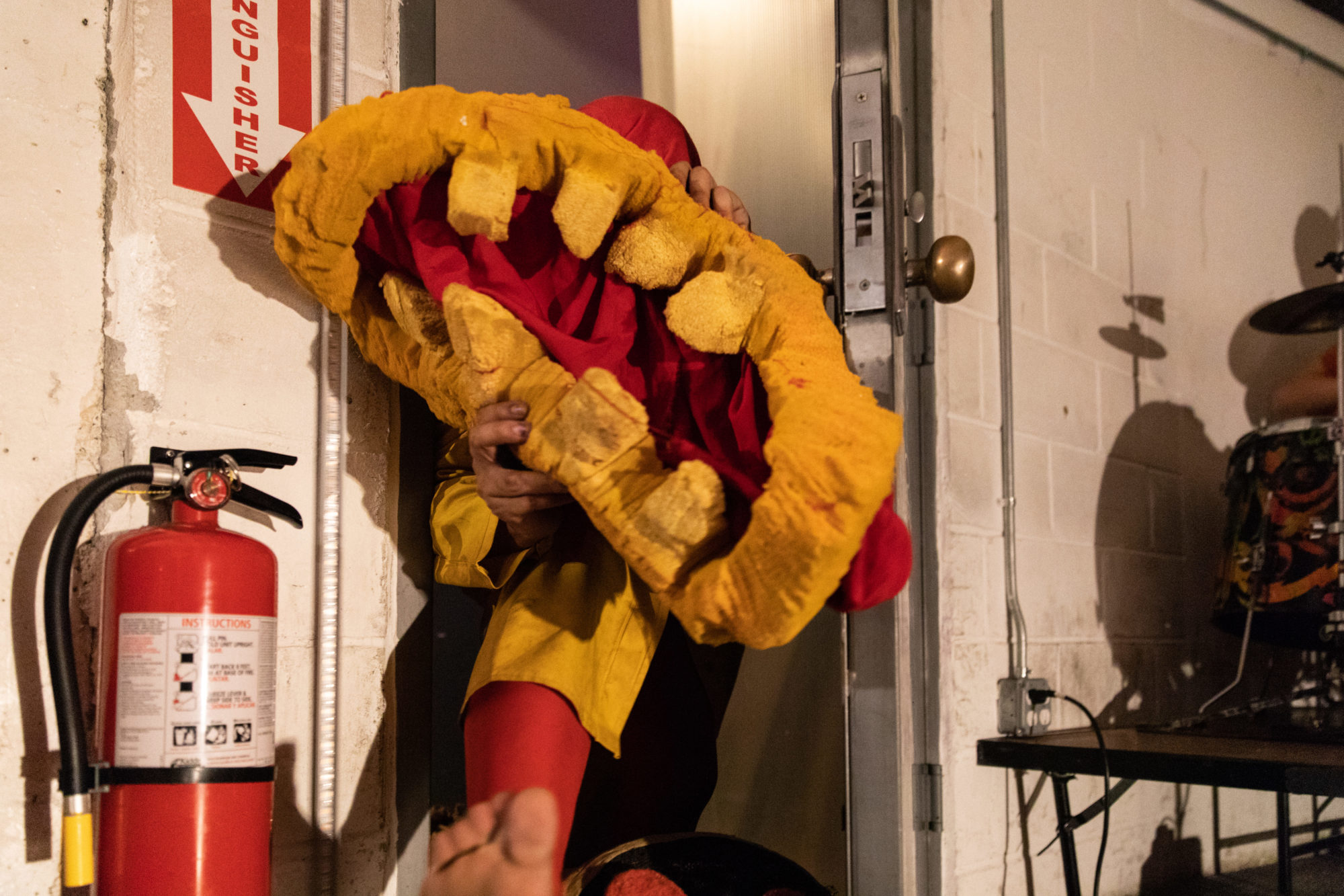 person dressed in red and yellow steps through a door holding a large red and yellow mouth