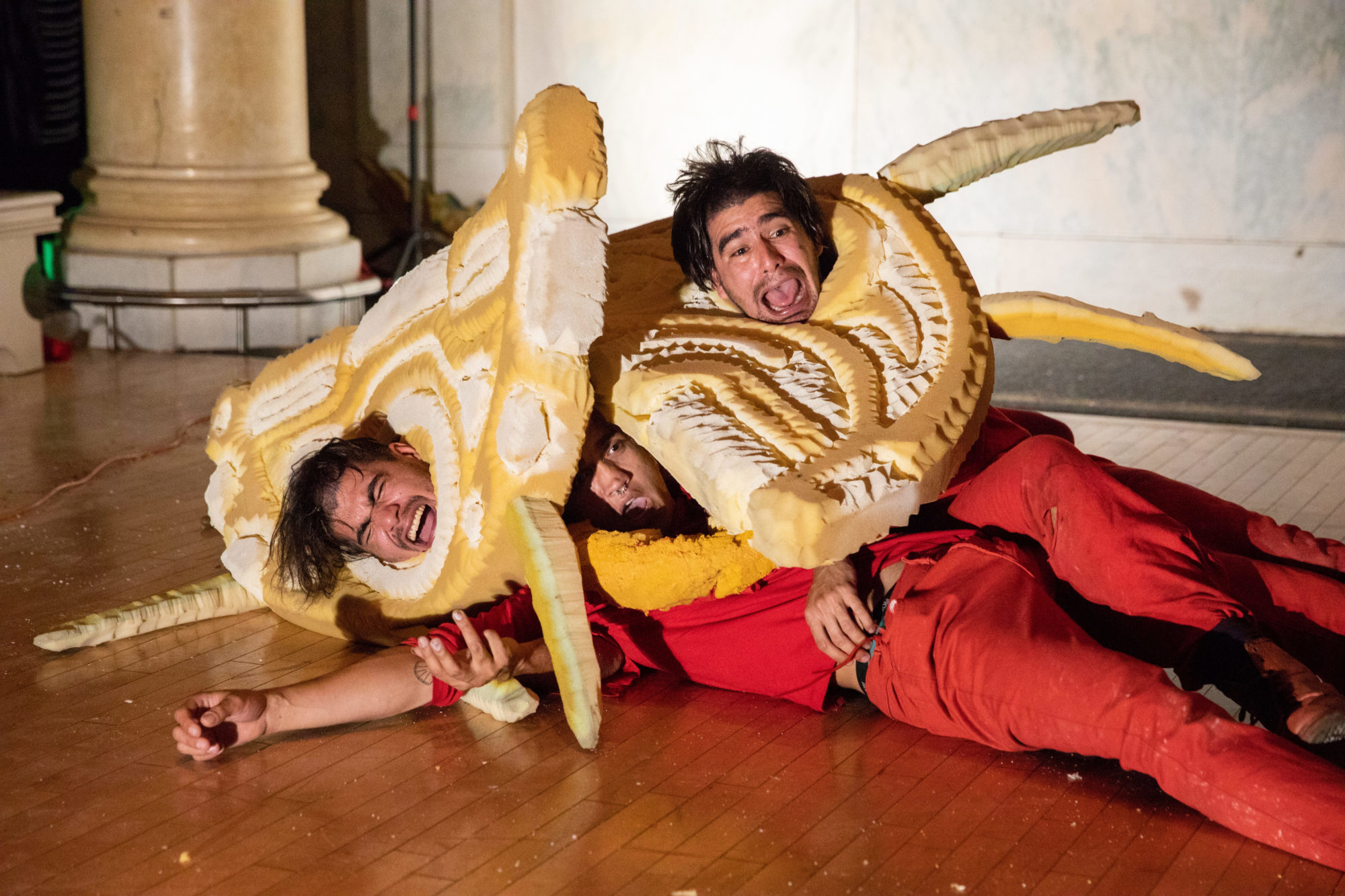 three people wearing red entangled on the floor, with their necks in a yellow foam structure