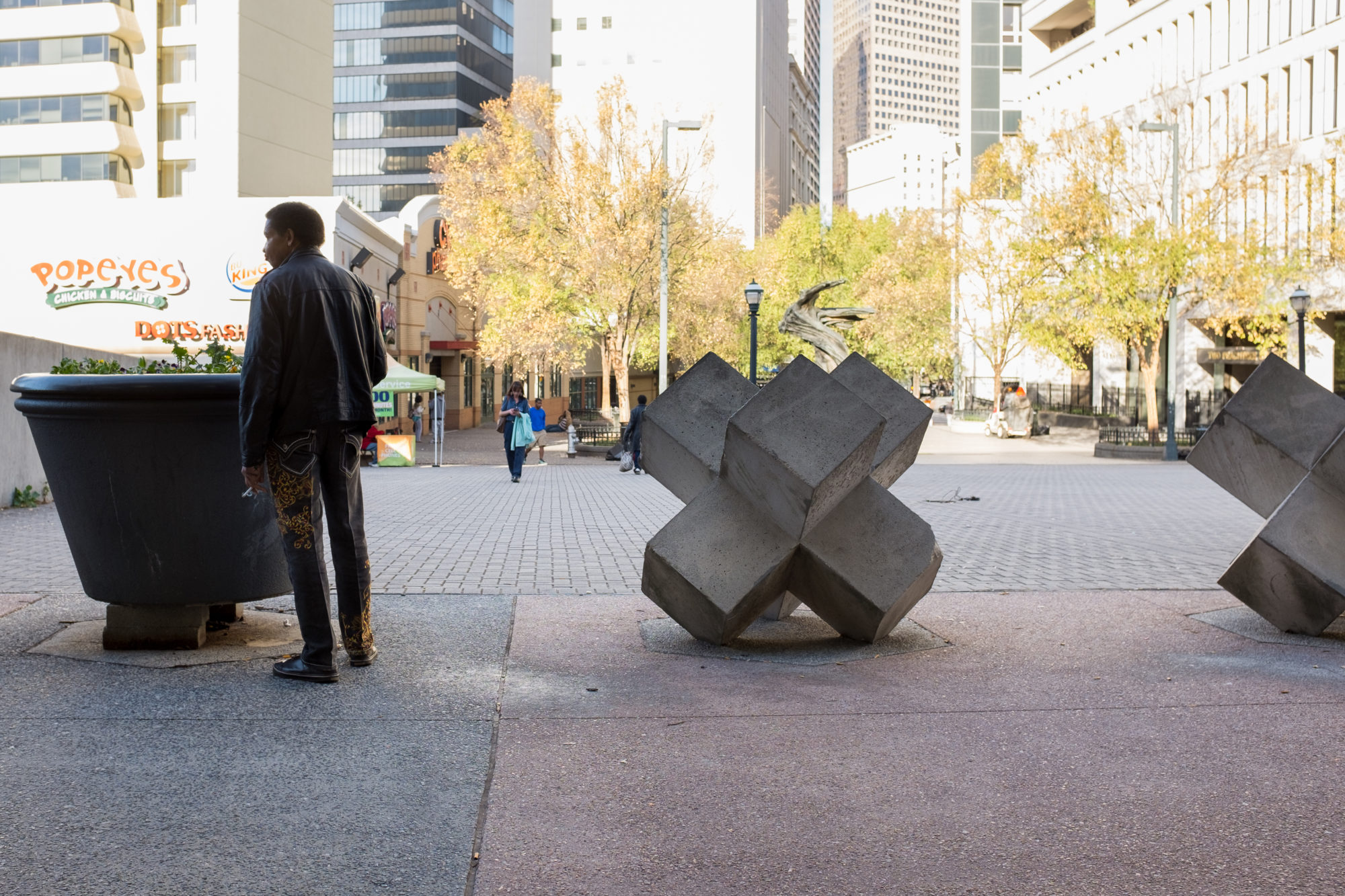A man stands between a planter and a cubic sculpture