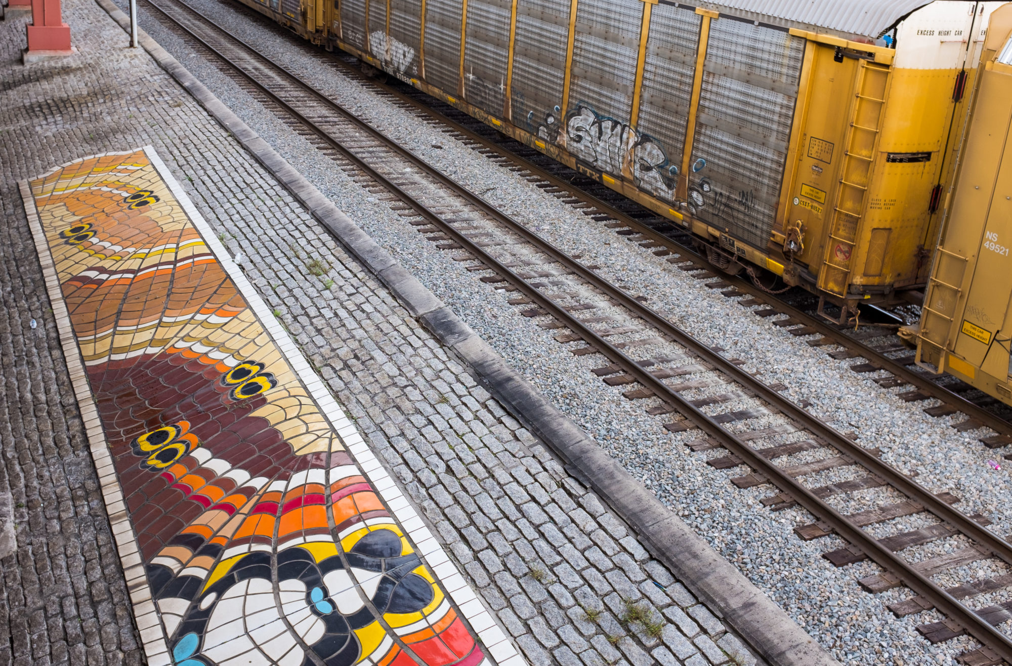 A colorful tile mural on cobblestone by train tracks