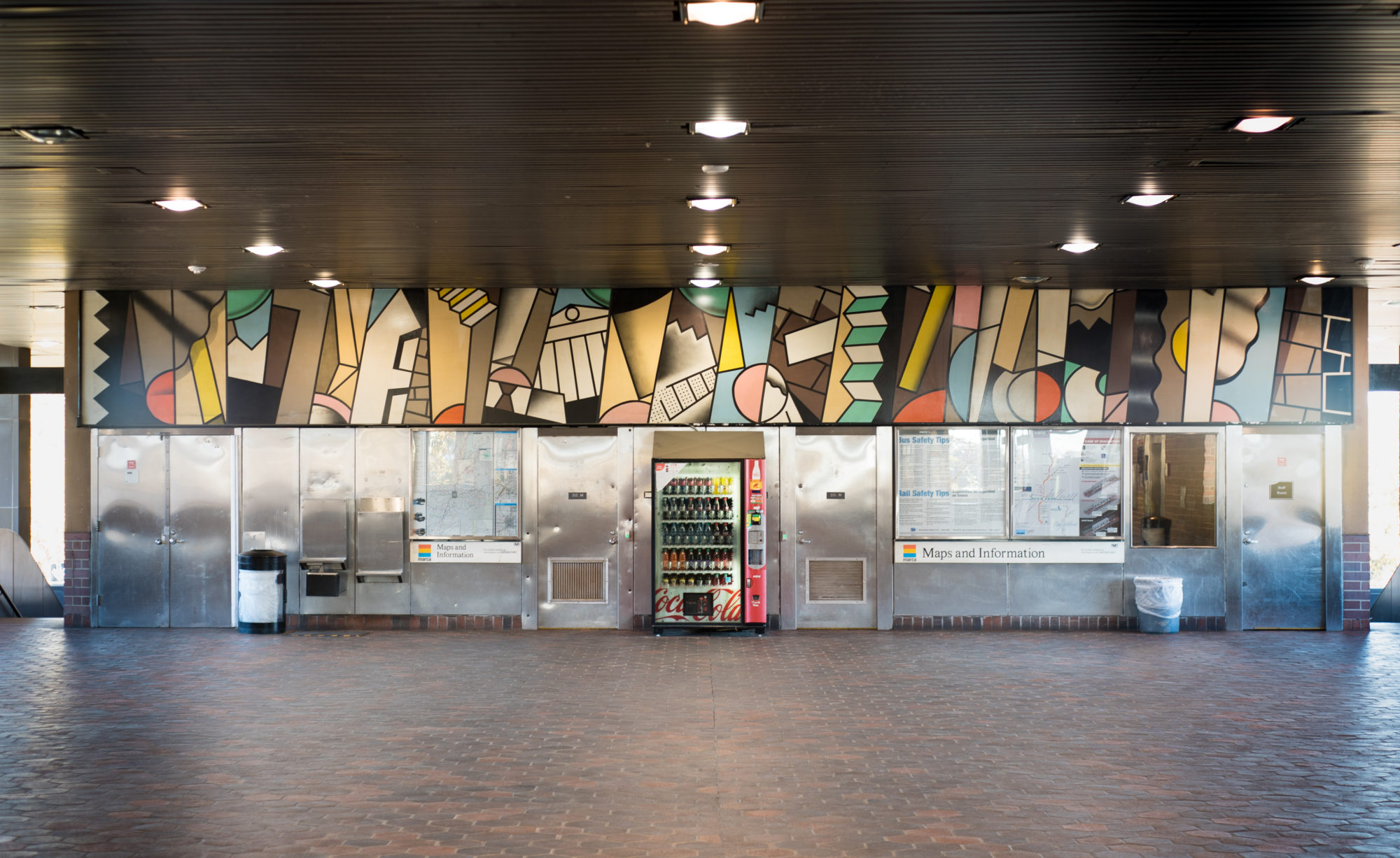 A colorful mural stretches along the ceiling, above the info desk and vending machine