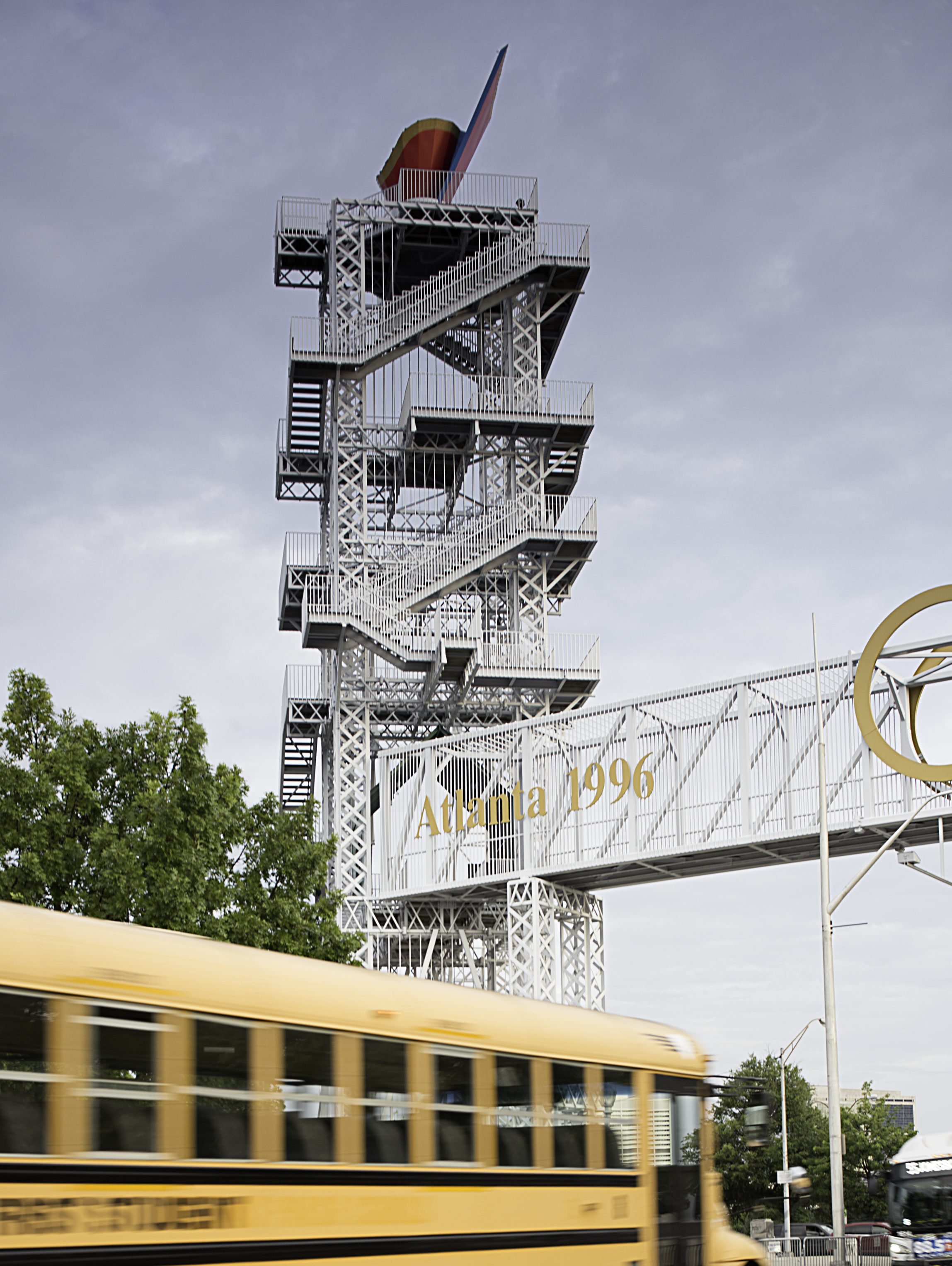 A closeup image of the Olympic Cauldron in Atlanta with a yellow school bus passing by, by Johnathon Kelso.