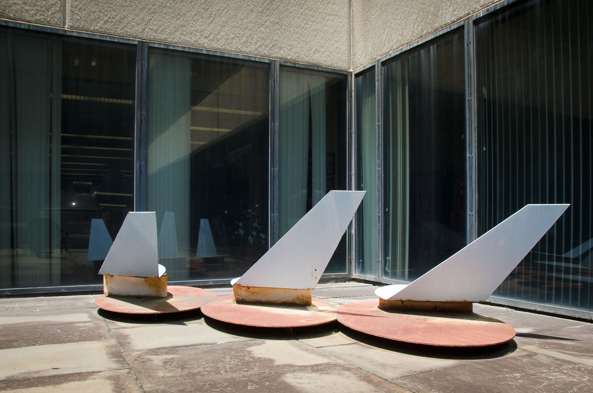 Three rusted, white sculptures in front of a building with large glass windows