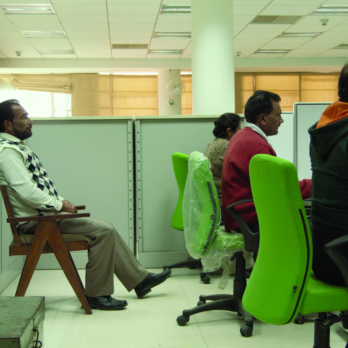 A video still from Amie Siegel's Provenance, 2013 featuring a group of people working in an office as one observes.