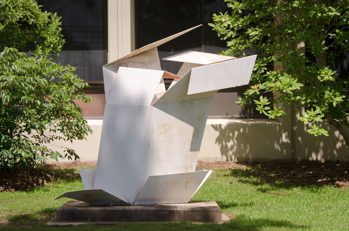 White sculpture surrounded by grass, trees, and a building