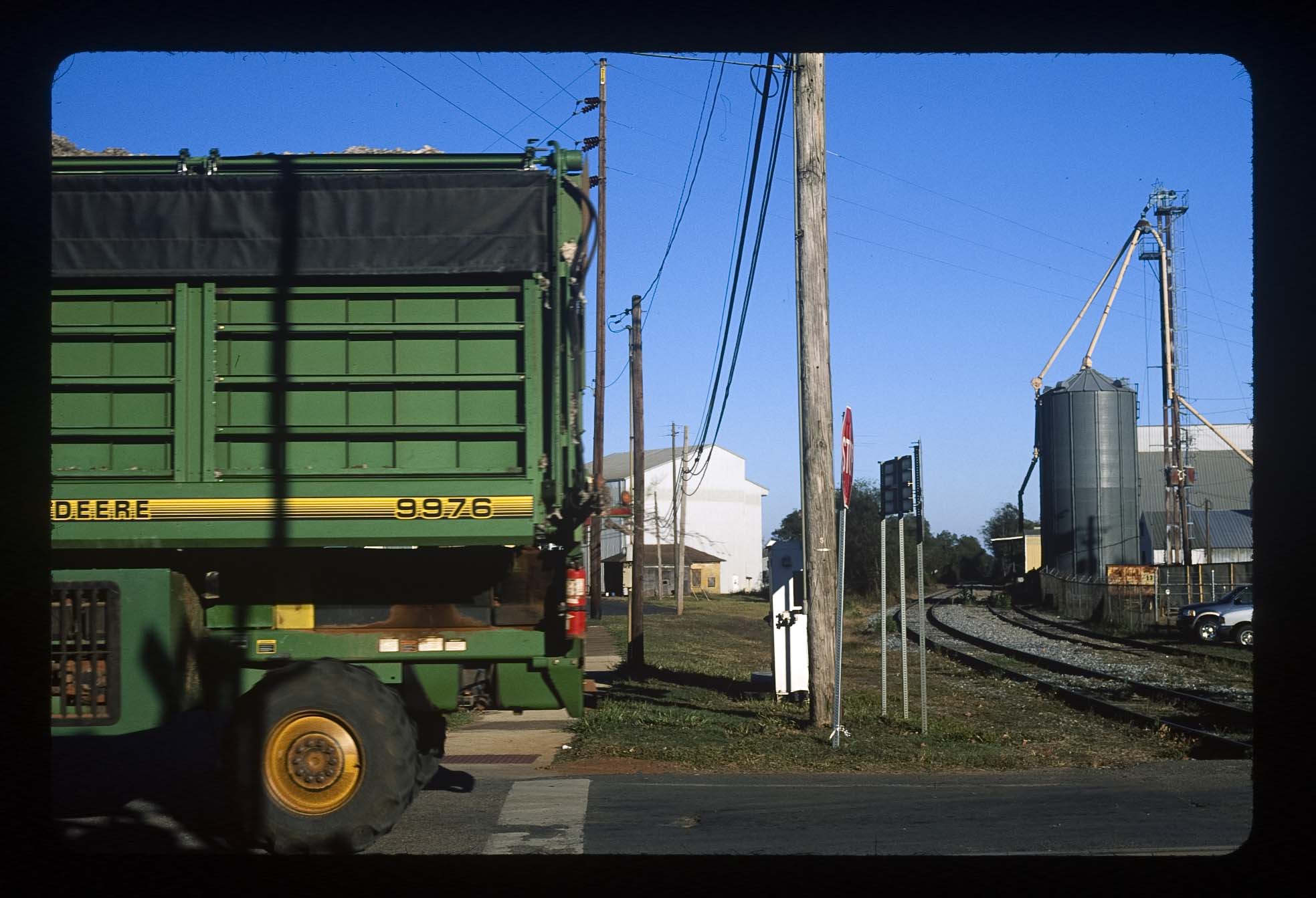 A green truck passing a factory and traintracks