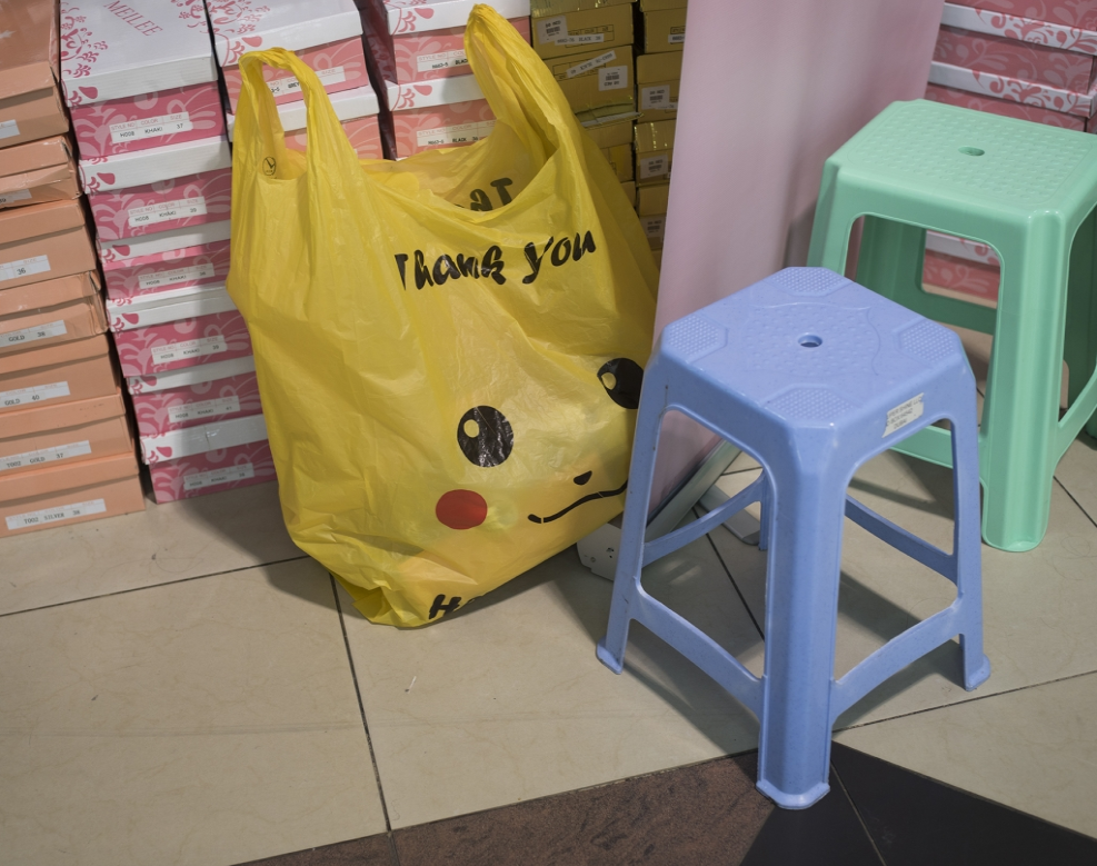 Yellow plastic shopping bag with Pikachu design sits in front of shoeboxes, next to a periwinkle step stool and mint green step stool.