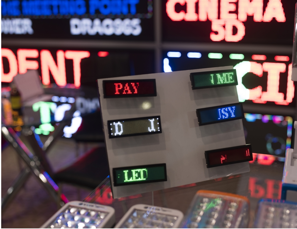Display of six small LED signs flashing fragments of words with several larger LED signs in the background.