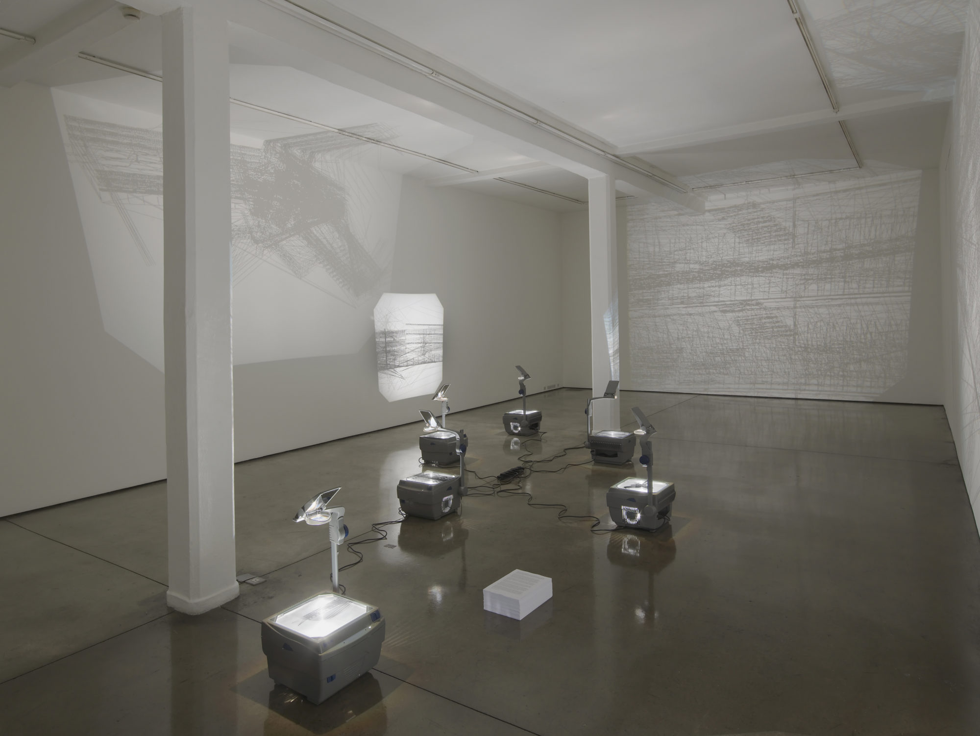 Multiple single image projectors sitting in a gallery space, displaying black and white architectural cad images.