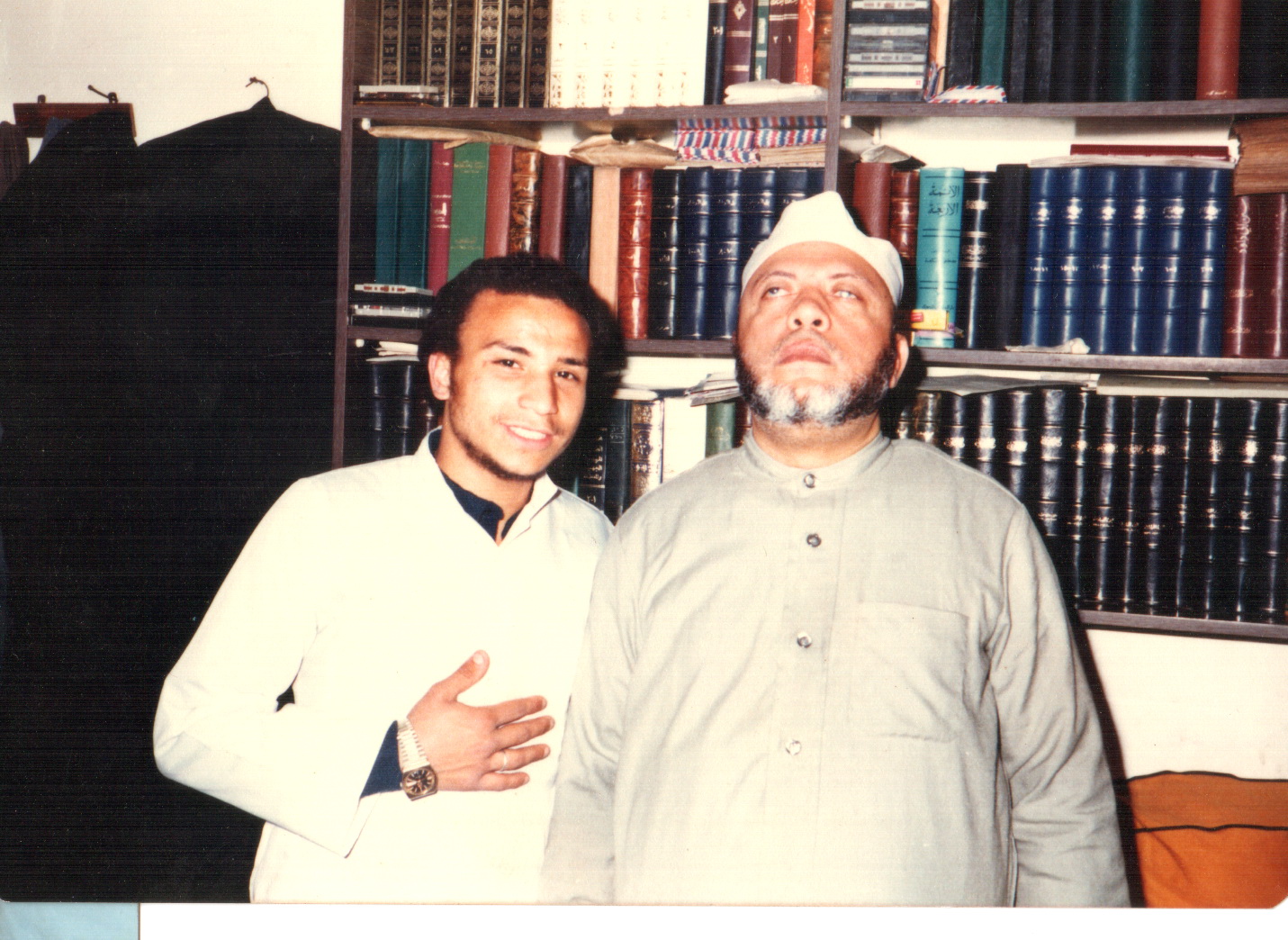 Two men stand in front of a bookshelf