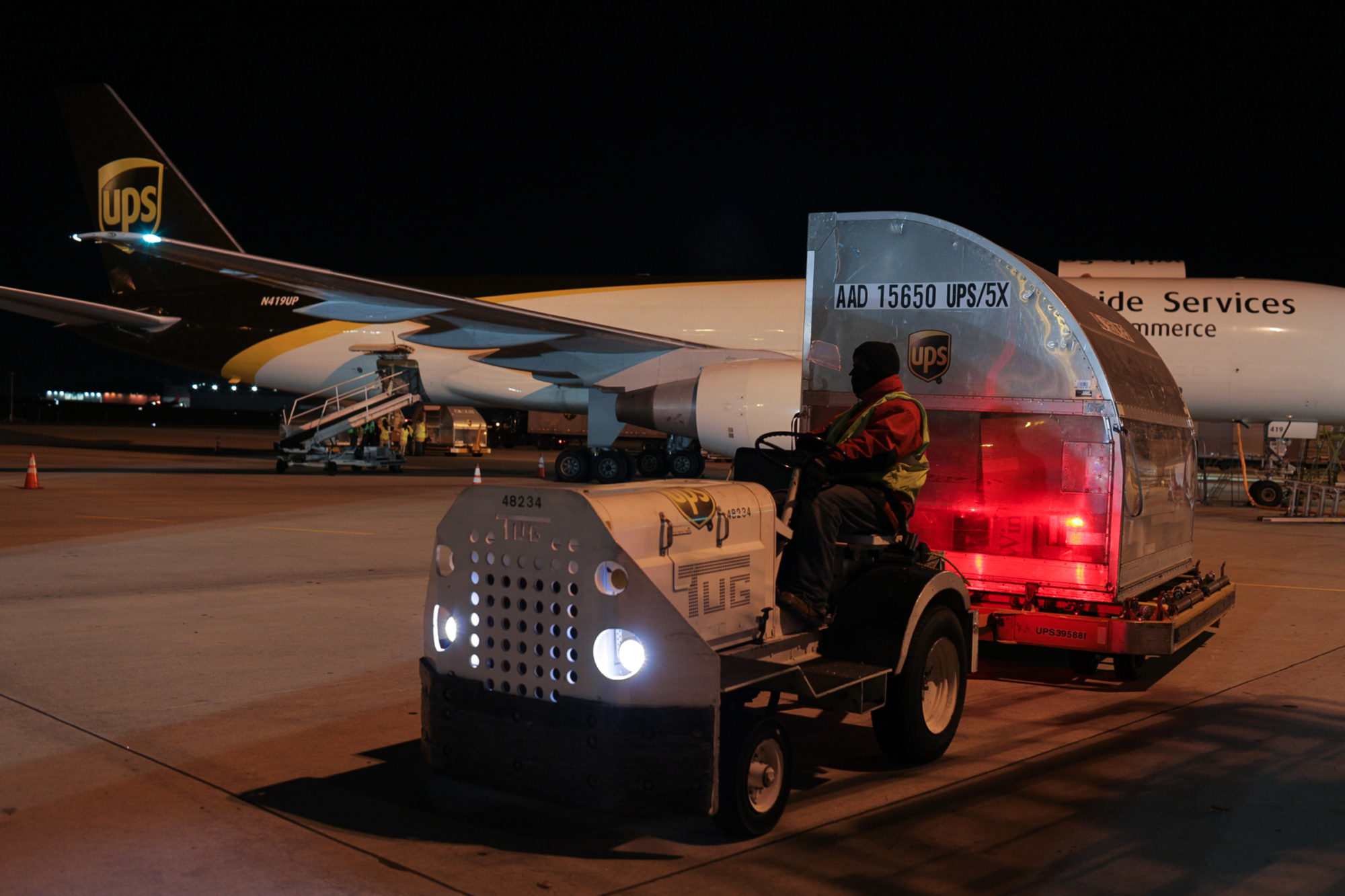 A UPS employee is using a vehicle in order to pull a container onto a UPS airplane