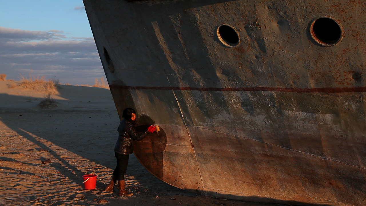 A figure dressed in all black and wearing red gloves, hand cleaning the front of a severely oxidized boat.