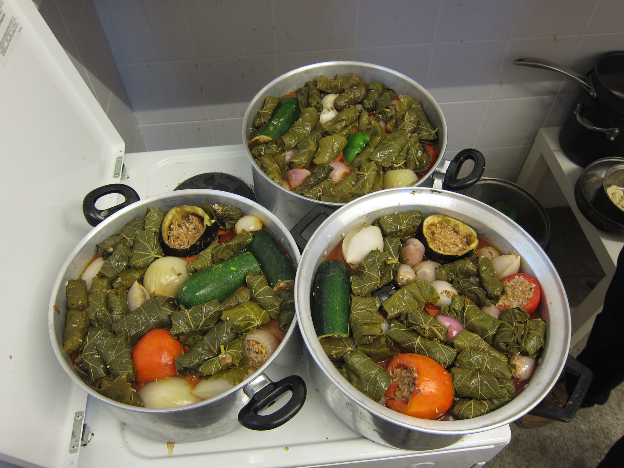 An image of three giant pots sitting on a stove, filled with green food.