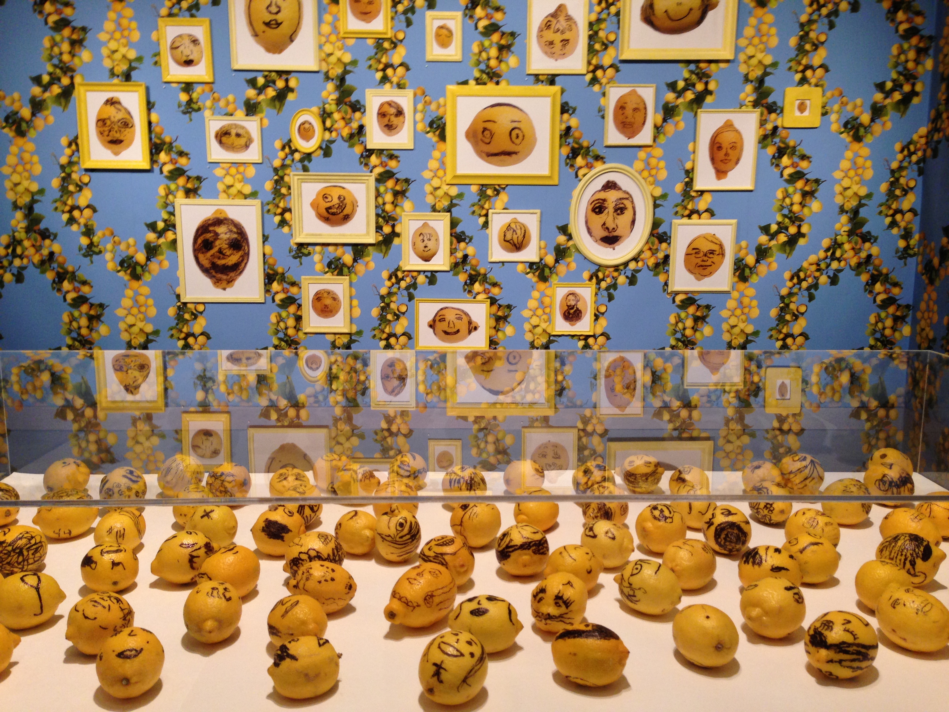 A bunch of lemons with faces drawn on them, sit's in a gallery