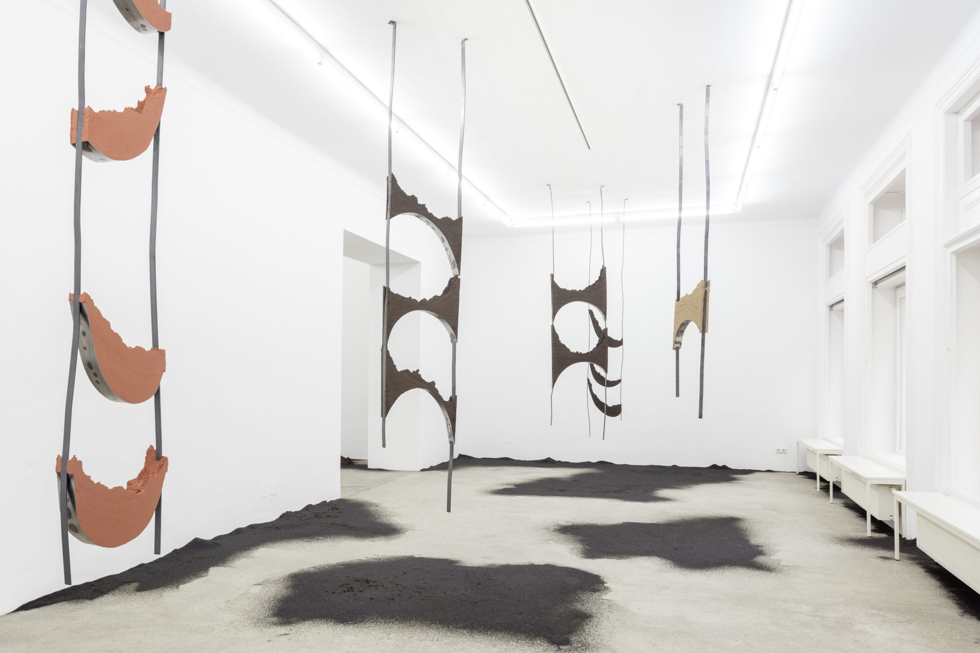 Five sculpture pieces hang from the ceiling in a gallery space