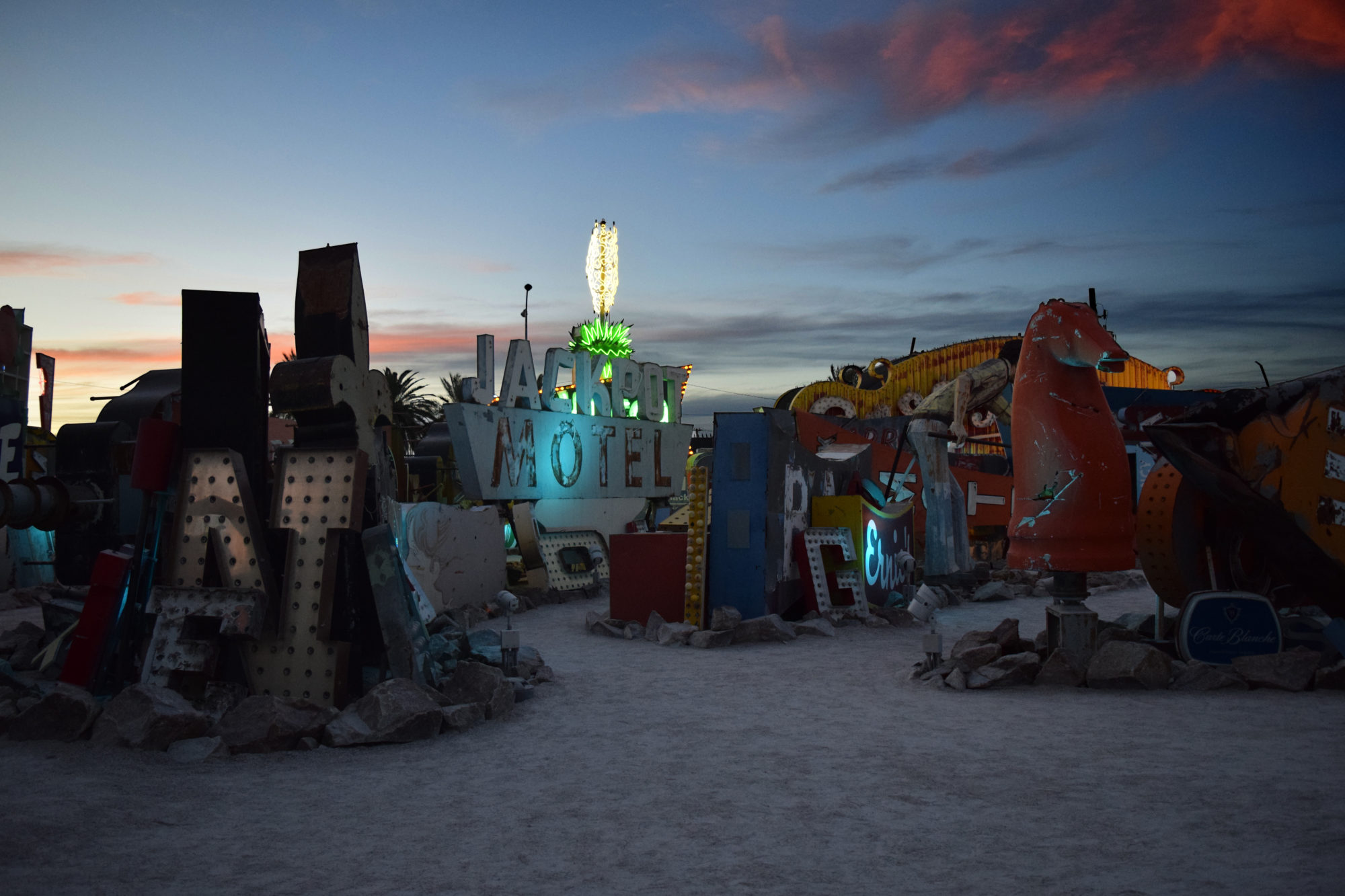 sculpture with various parts, colorful and llit with different letters, figures and colors blue sky and red clouds, sunset