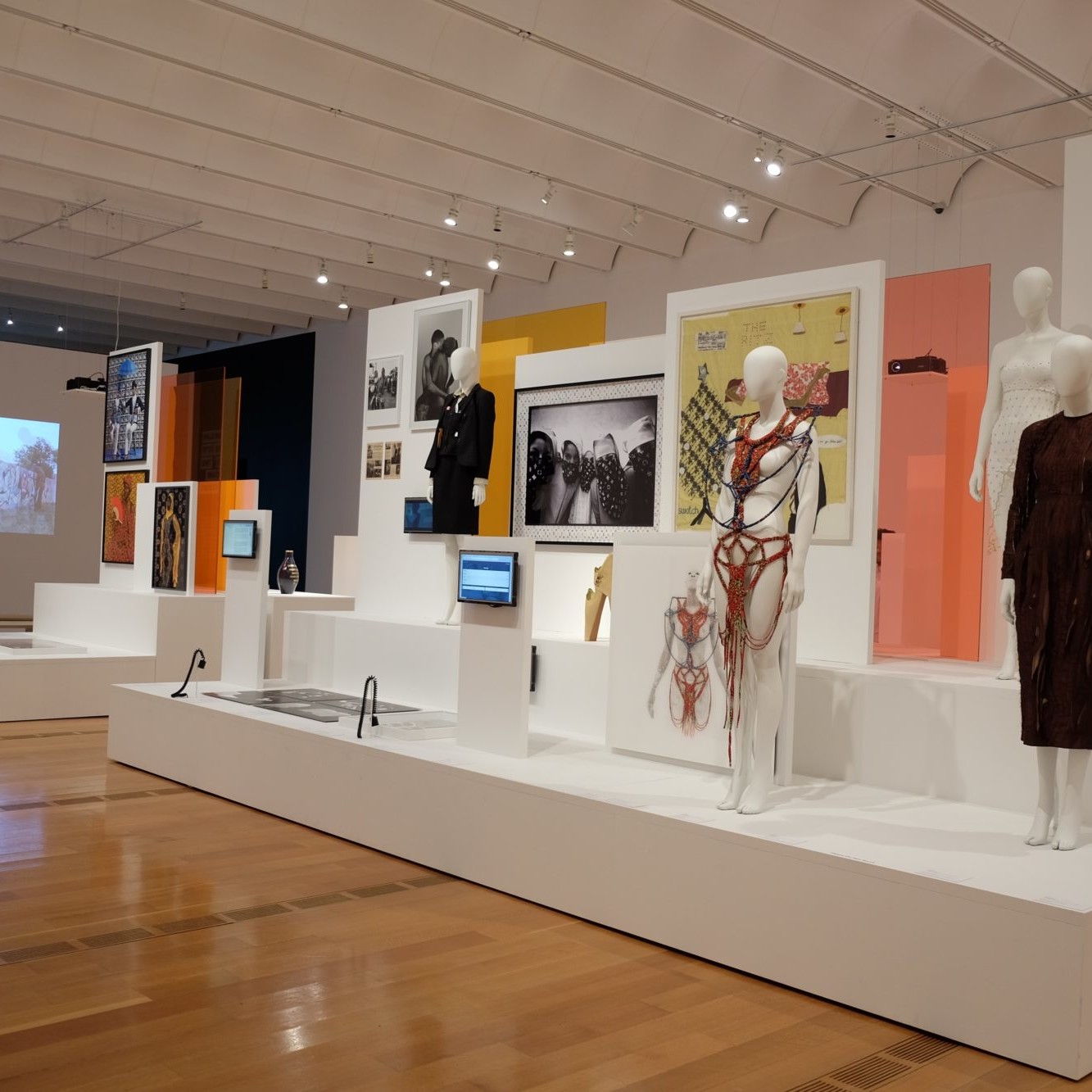 Mannequins wear various fashion designs in a large gallery with wood panel floors