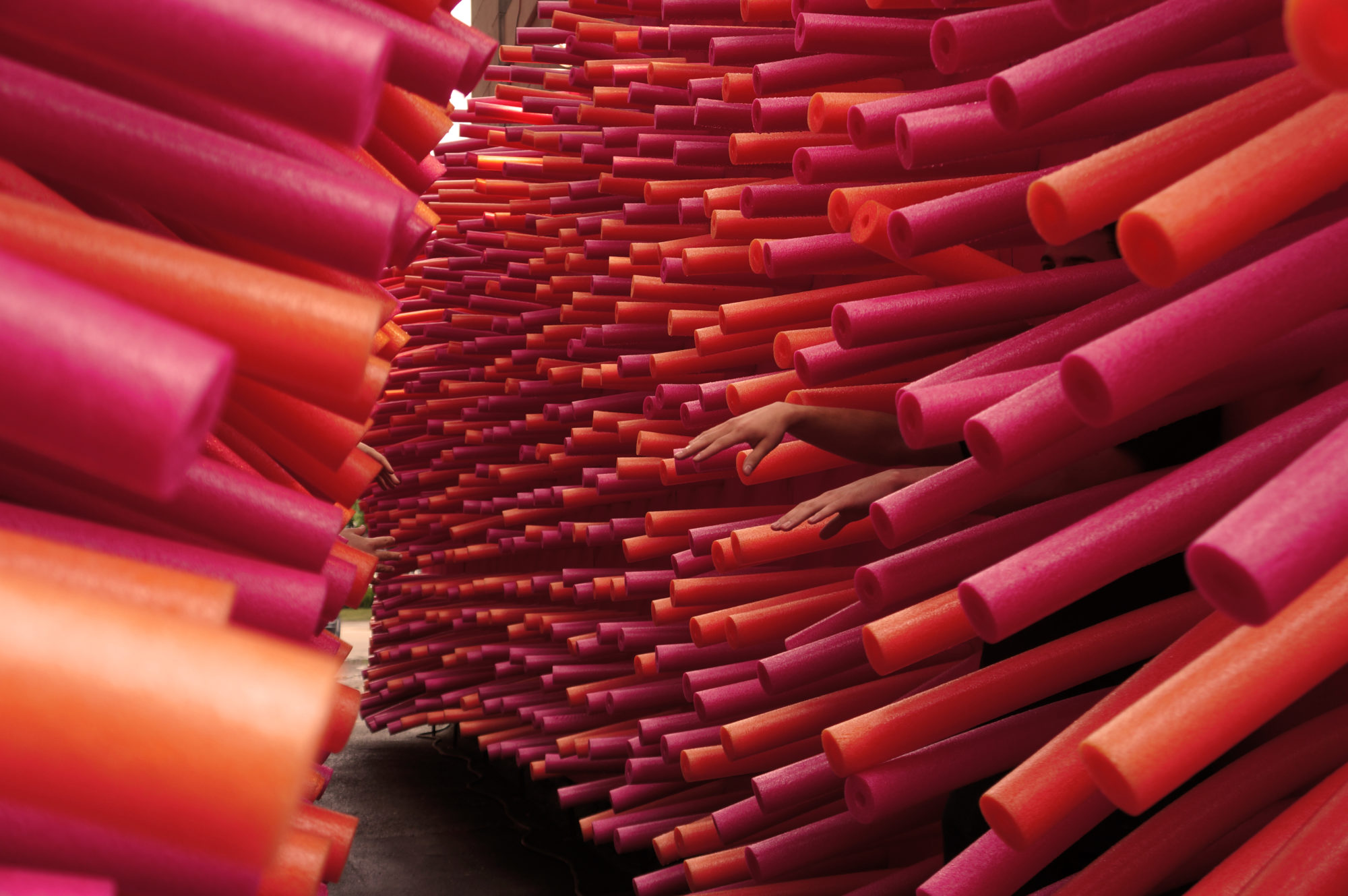 Two pairs of hands stick out of a bunch of pink and orange pool noodles