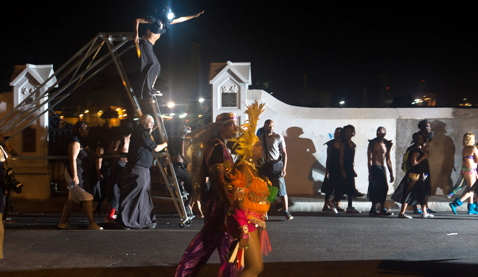 People wearing matching all-black outfits or carnival outfits walk down a street at night