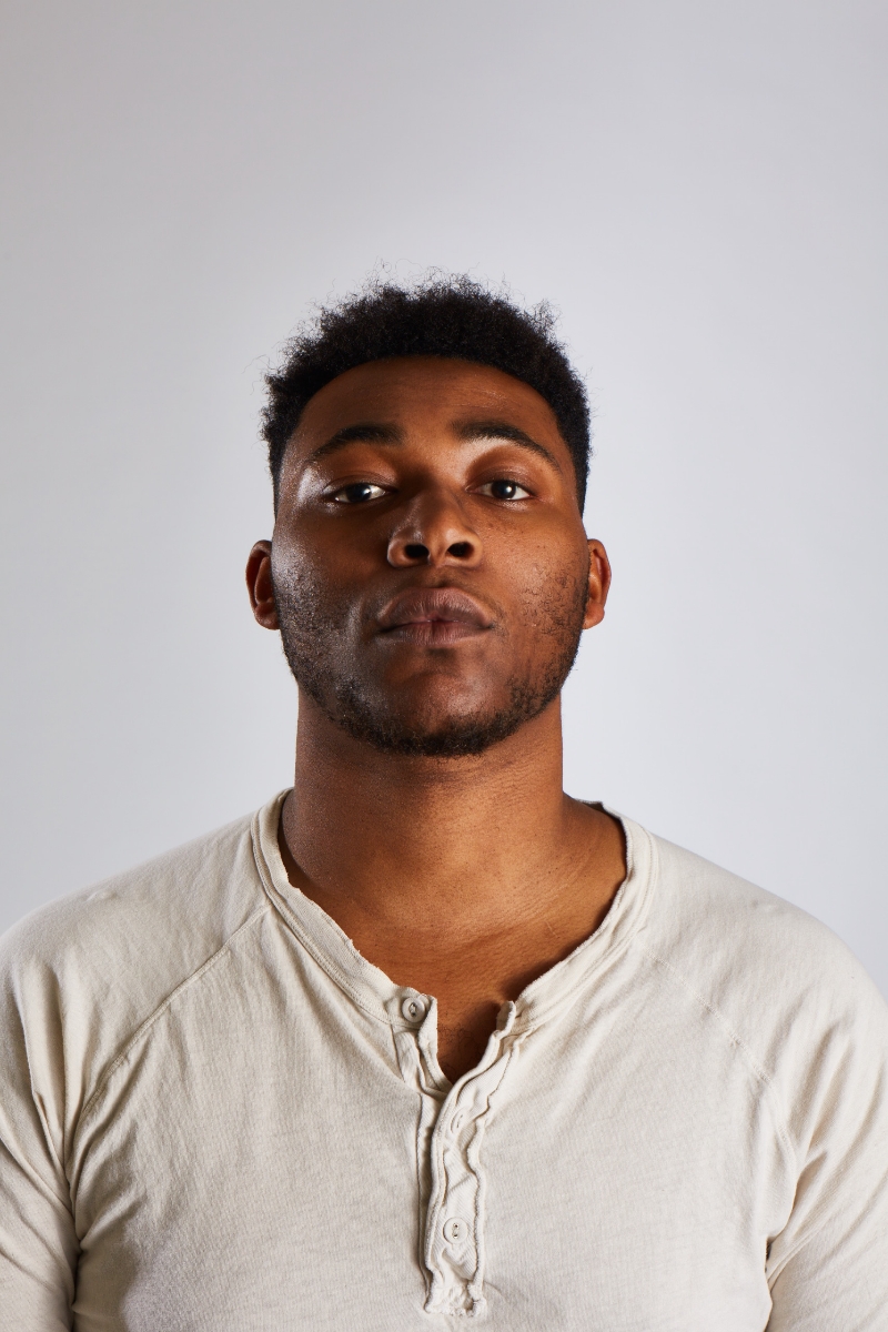 A straight-on photograph of a man in a white henley. He looks slightly upwards at the camera.