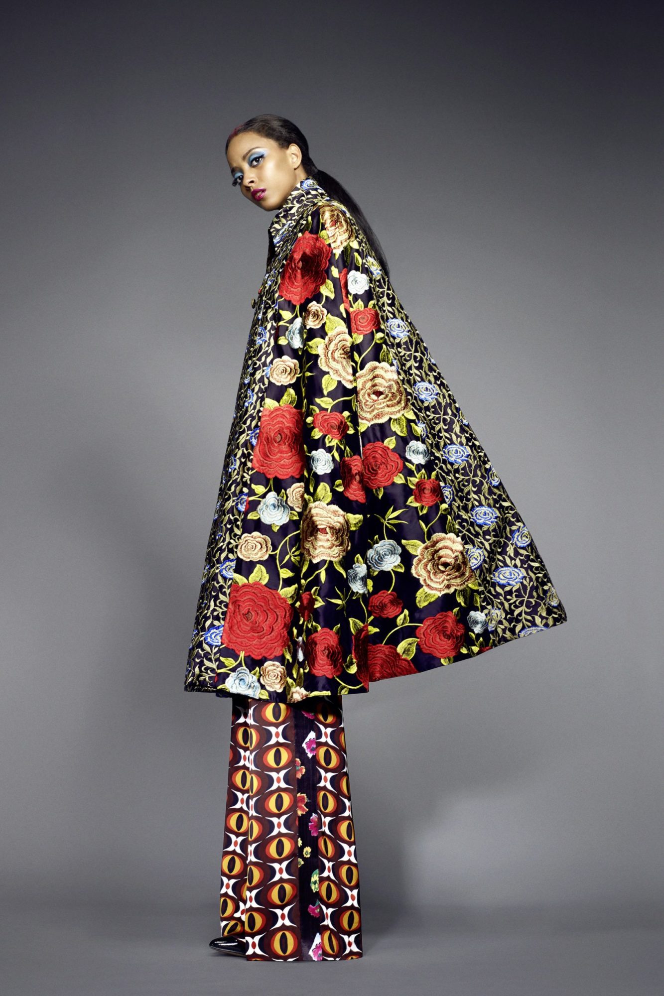 Model wearing oversized coat and pants with bright floral and geometric patterns