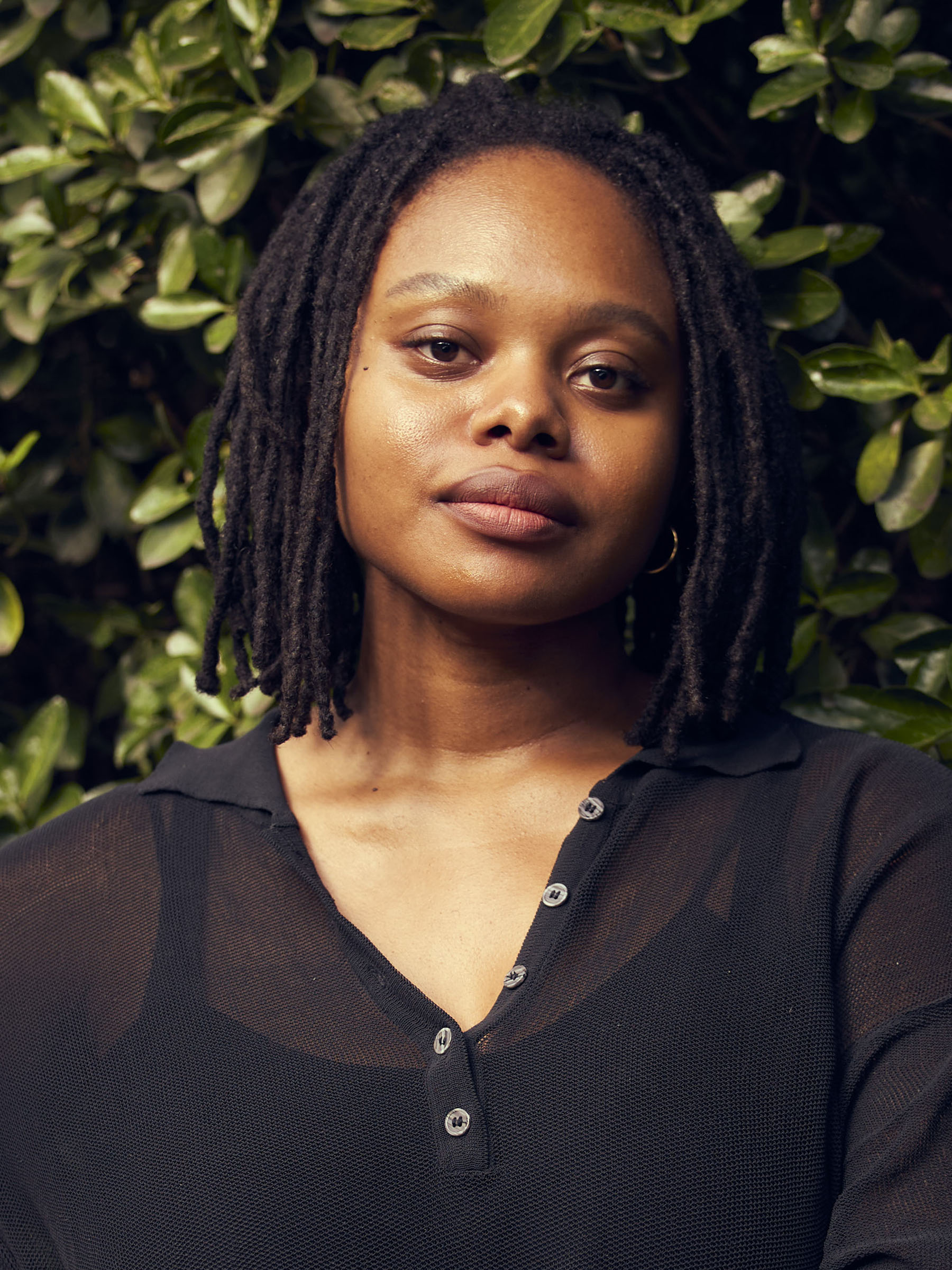 Contributing editor Re'al Christian faces directly into the camera for this portrait taken of her; in the background there is green foilage.