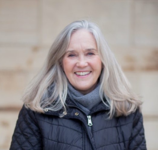 A woman wearing a winter jacket stands outside, smiling.