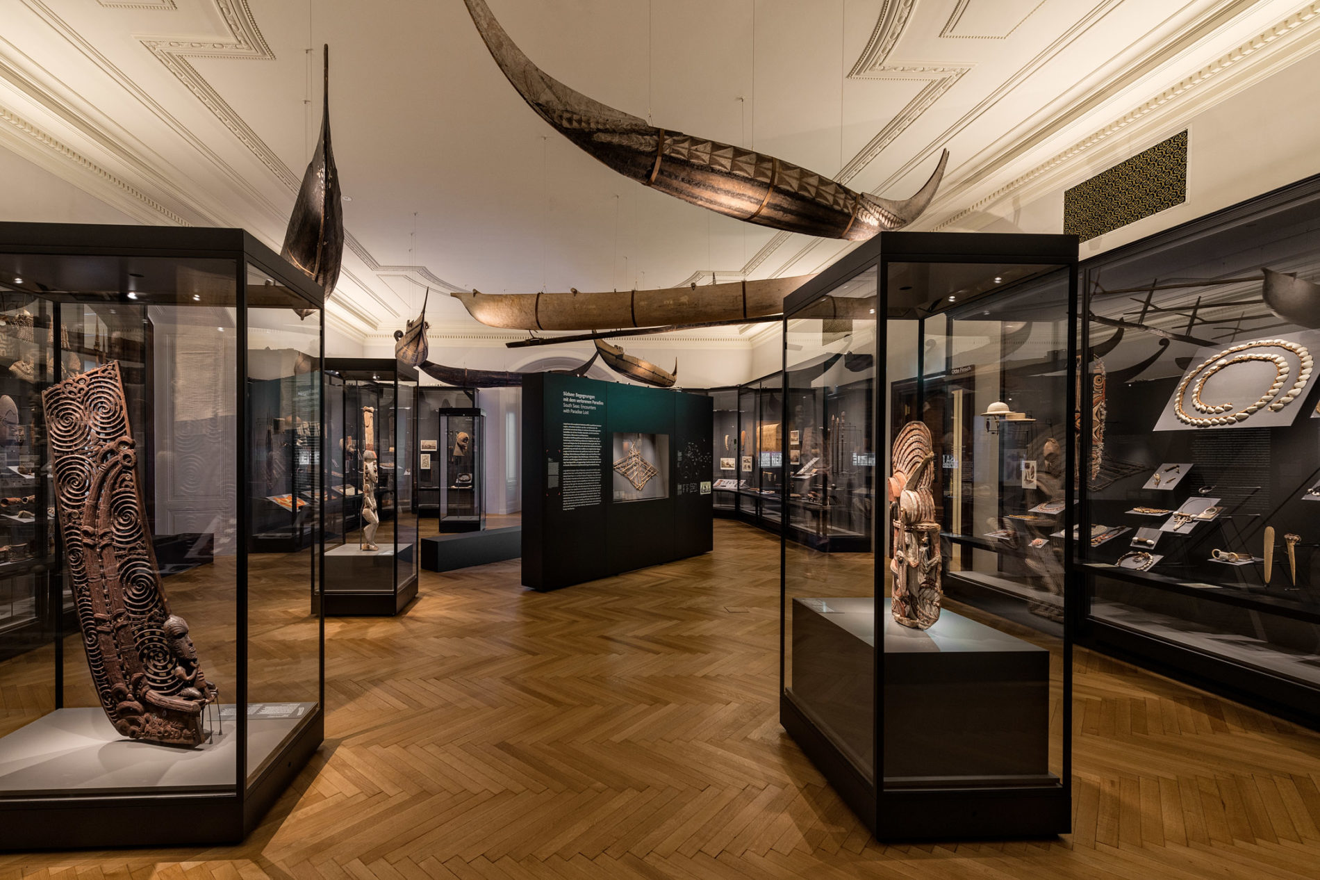 exhibition with wooded statues and canoes in white room with black cases