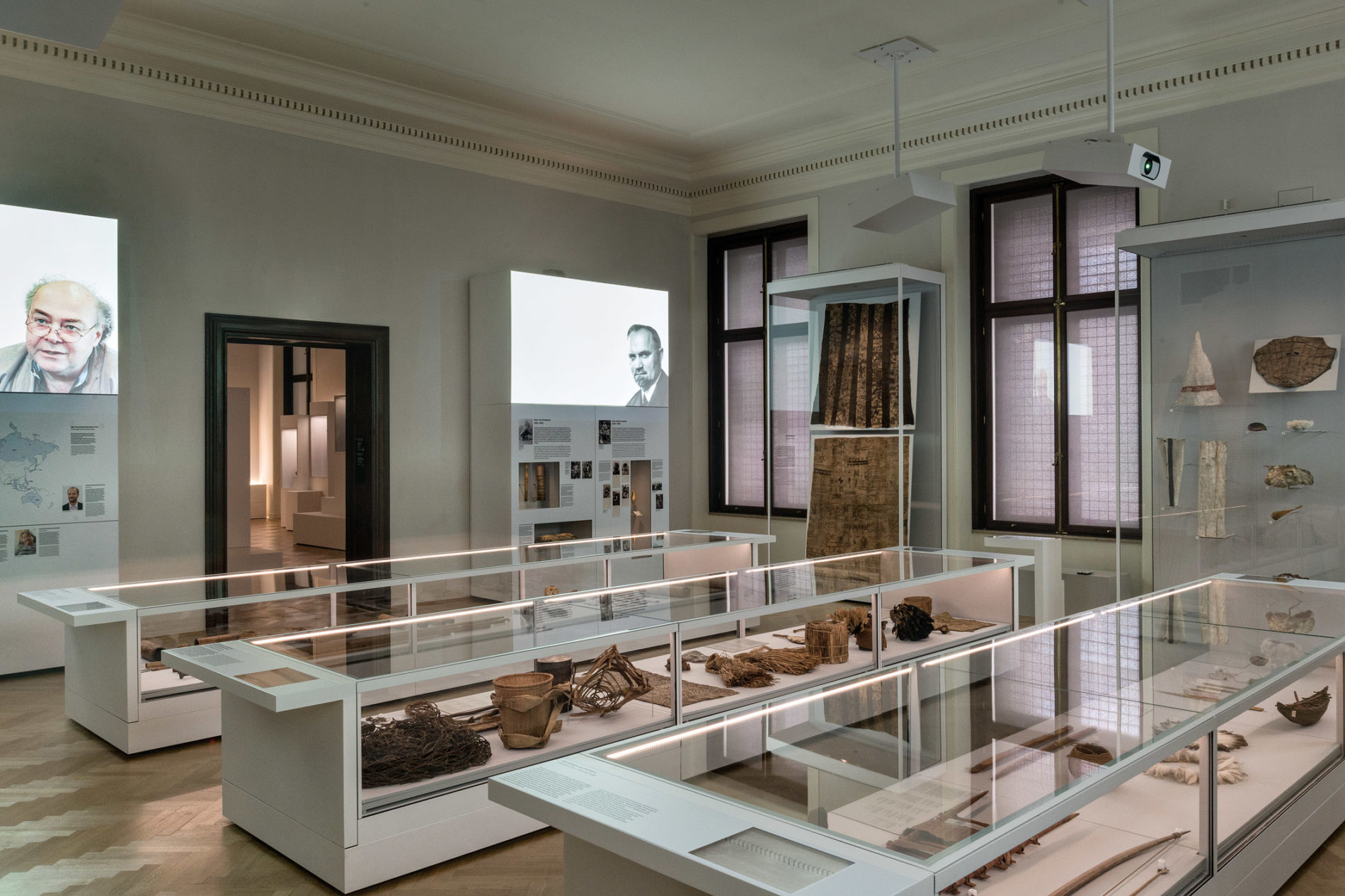 exhibition in white room with brown and black artifacts and video projections