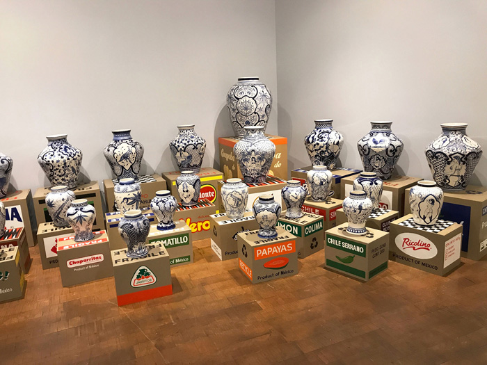 A variety of vases in the style of blue and white pottery stand on boxes bearing the names and logos of popular brands