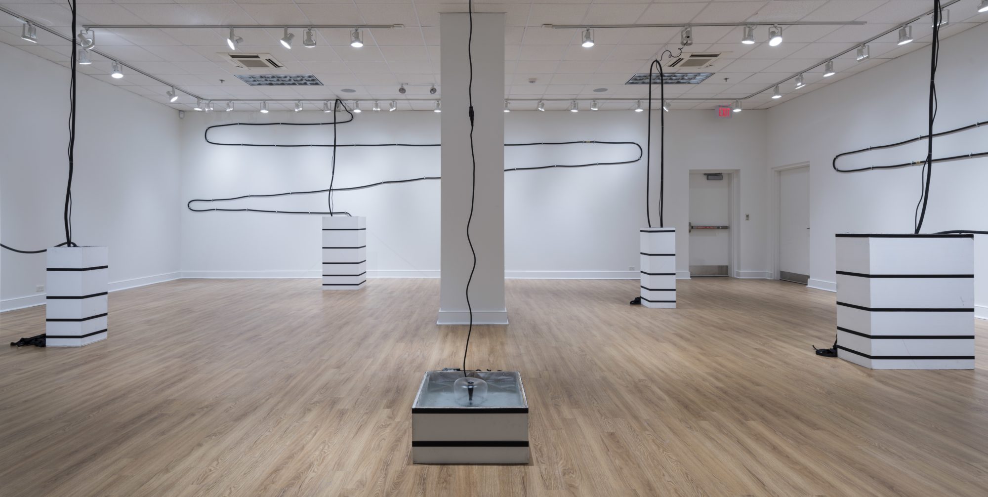 Several black and white sculptural installations featuring wires by Virginia Overton are shown in a large gallery space with white walls and ceiling and a light-colored wood floor.