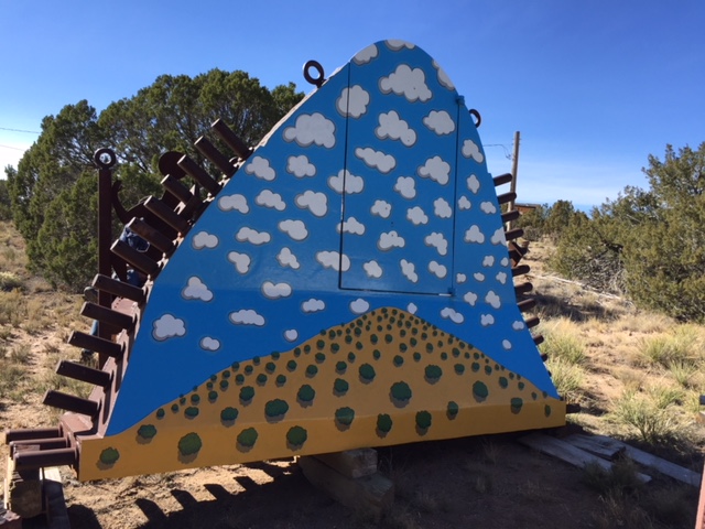 large steel fragment painted with clouds and a desert