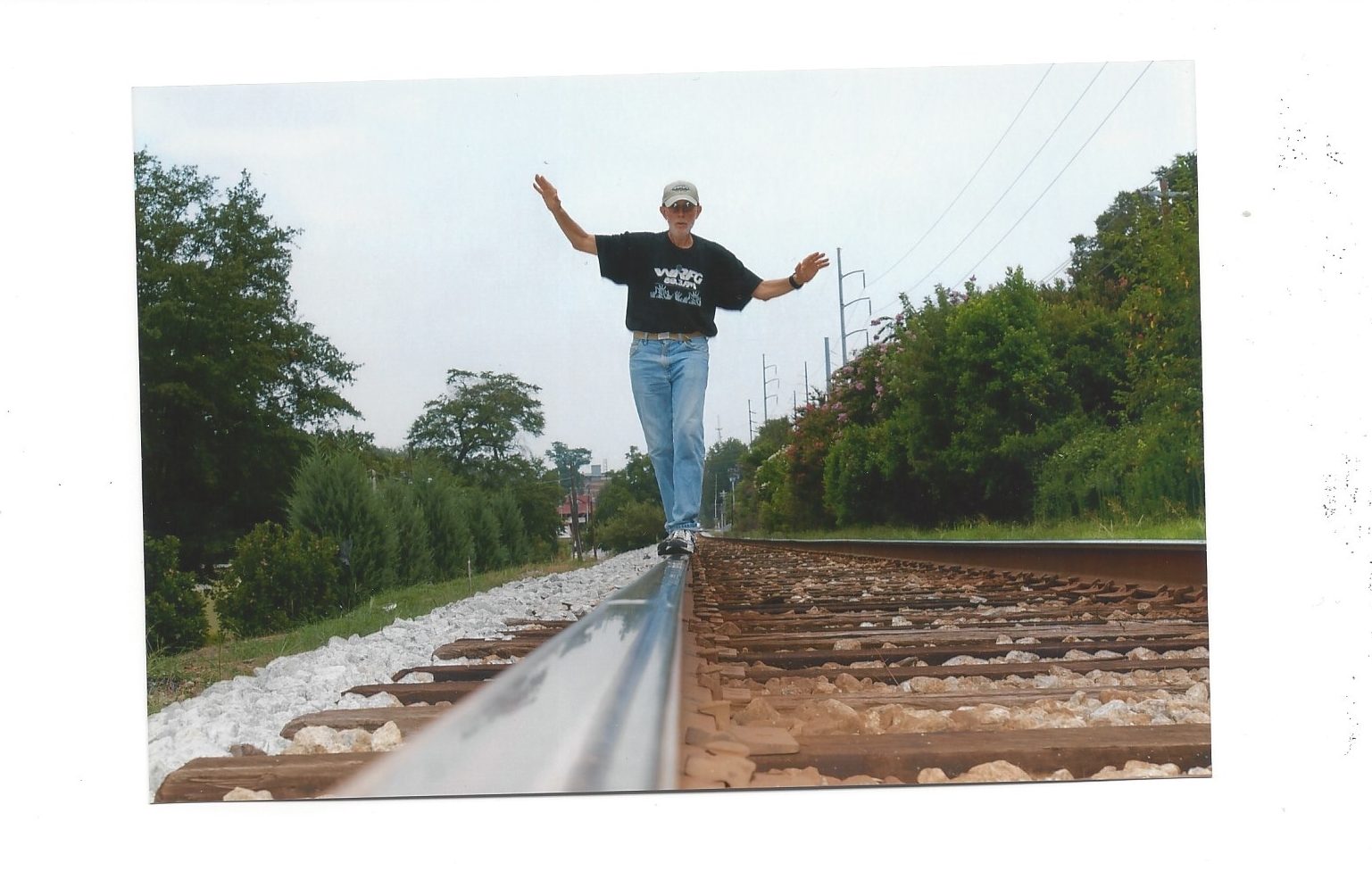 Brian Sherman, wearing blue jeans and black shirt while walking on train tracks