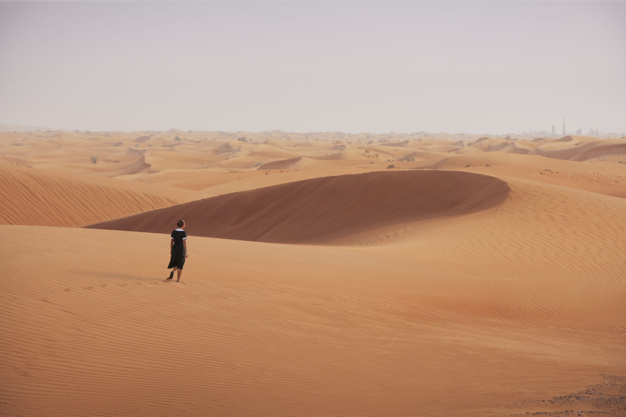 woman in a black and white outfit walks through far-stretching orange sand dunes