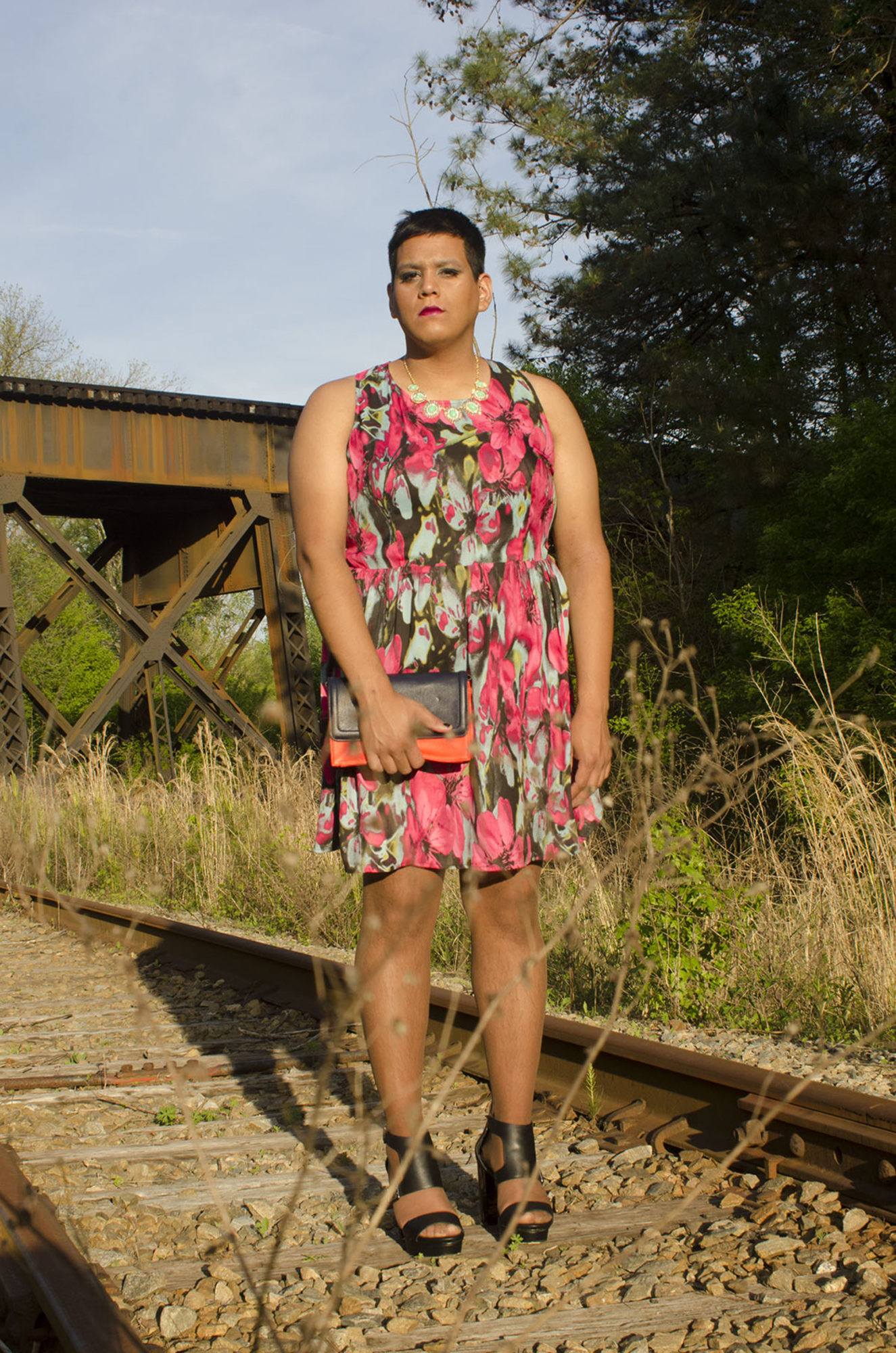 A person stands in a floral dress on train tracks