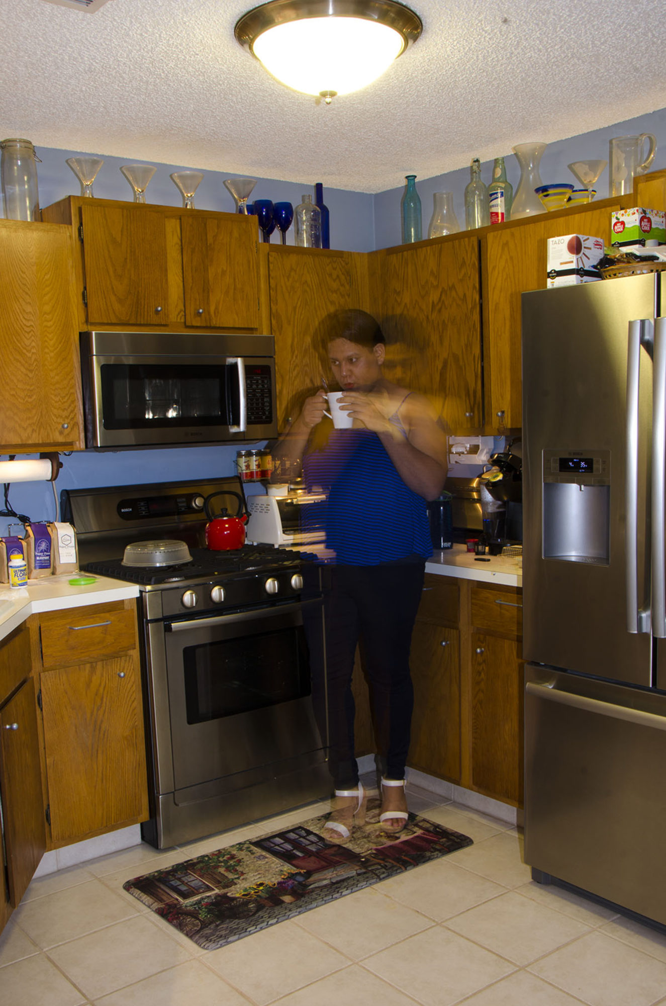 A blurred woman drinks coffee in a kitchen