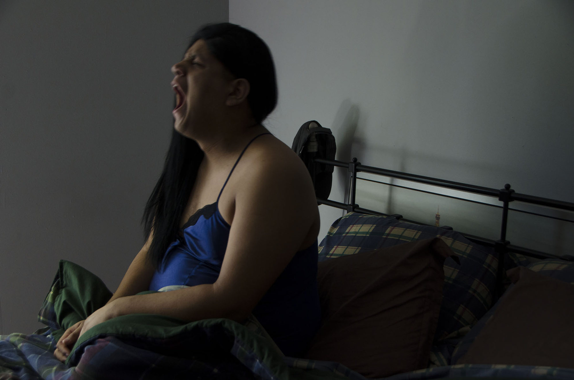 A woman sits in bed, either yelling, or yawning