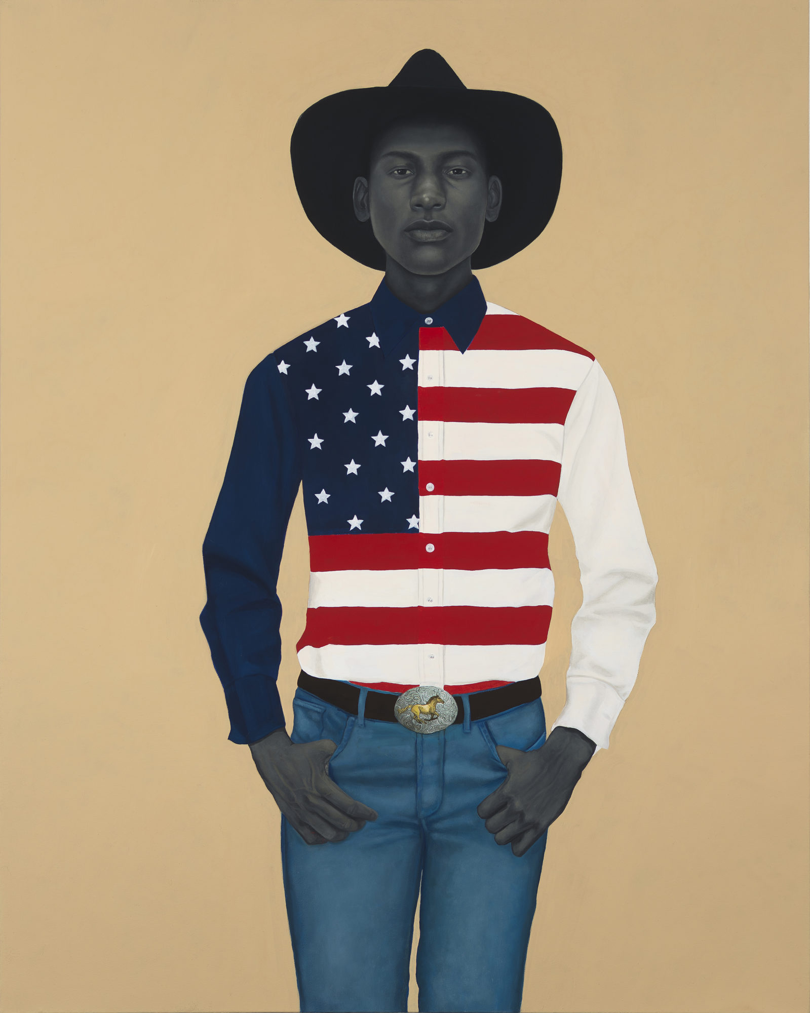 A man in a cowboy hat and an American flag button up shirt stands in front of a tan background
